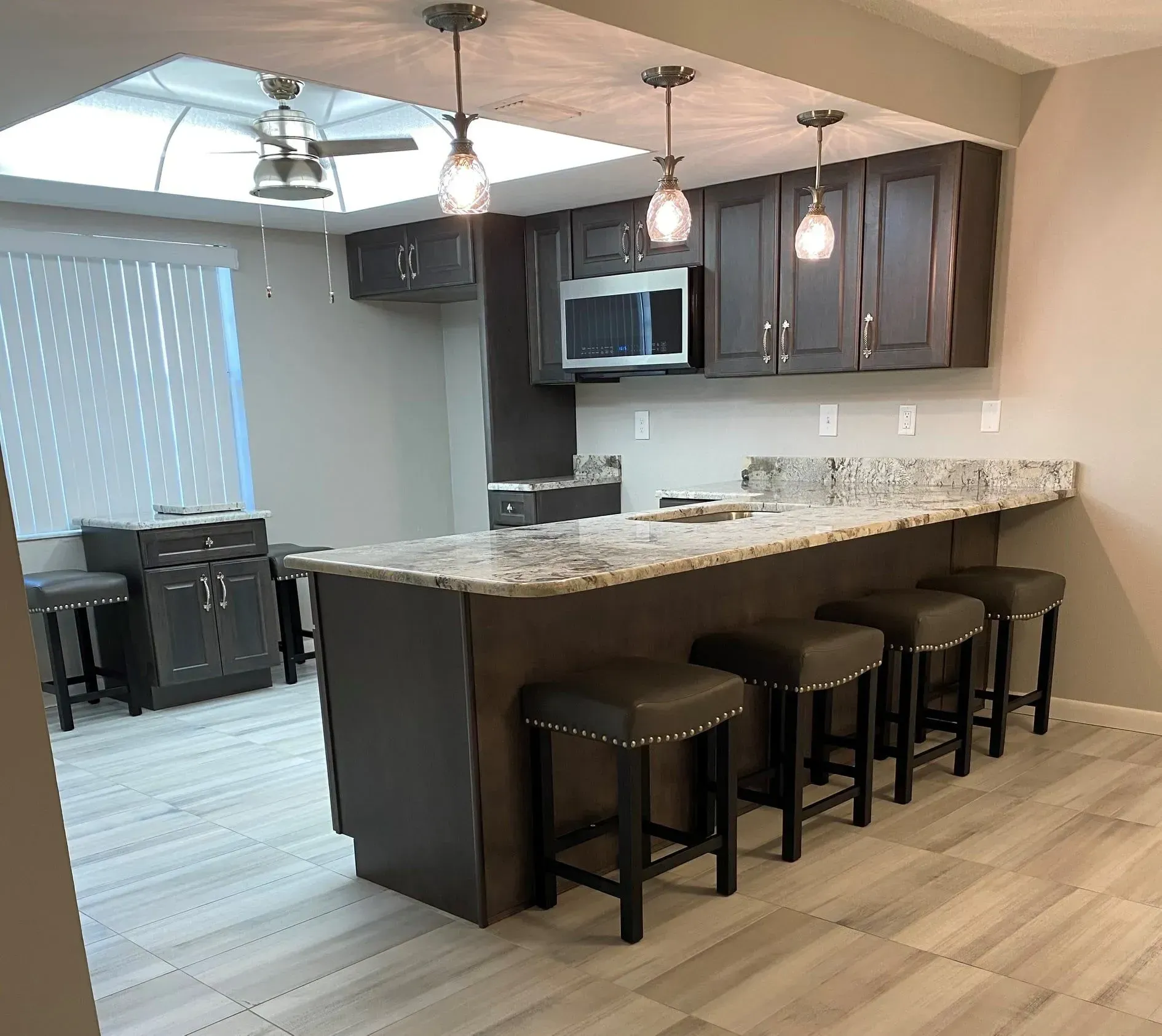 Modern kitchen with dark brown cabinets, granite countertops, and a breakfast bar with stools.