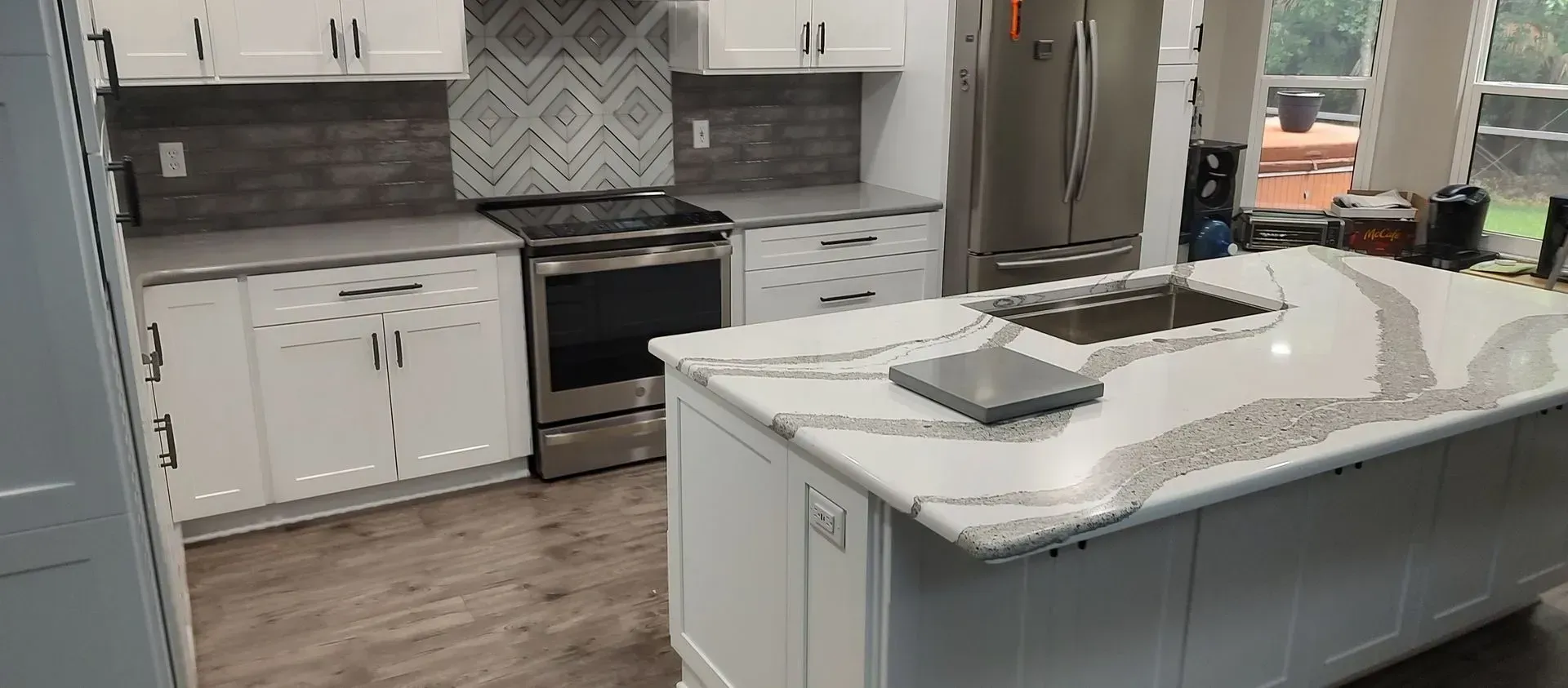 Modern kitchen with white cabinets, stainless steel appliances, and a quartz countertop island.