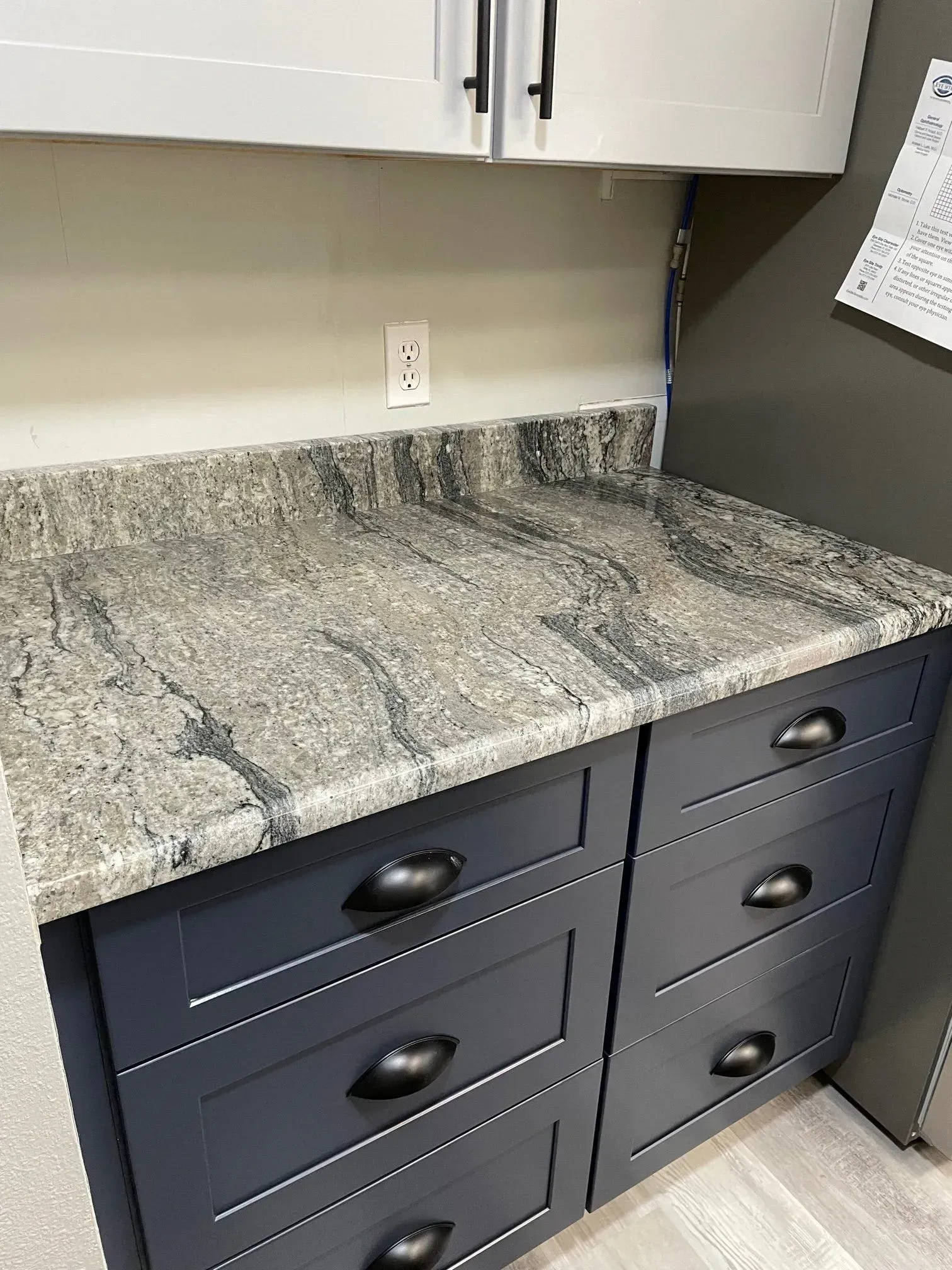 Gray speckled countertop on navy blue kitchen cabinets with black handles.