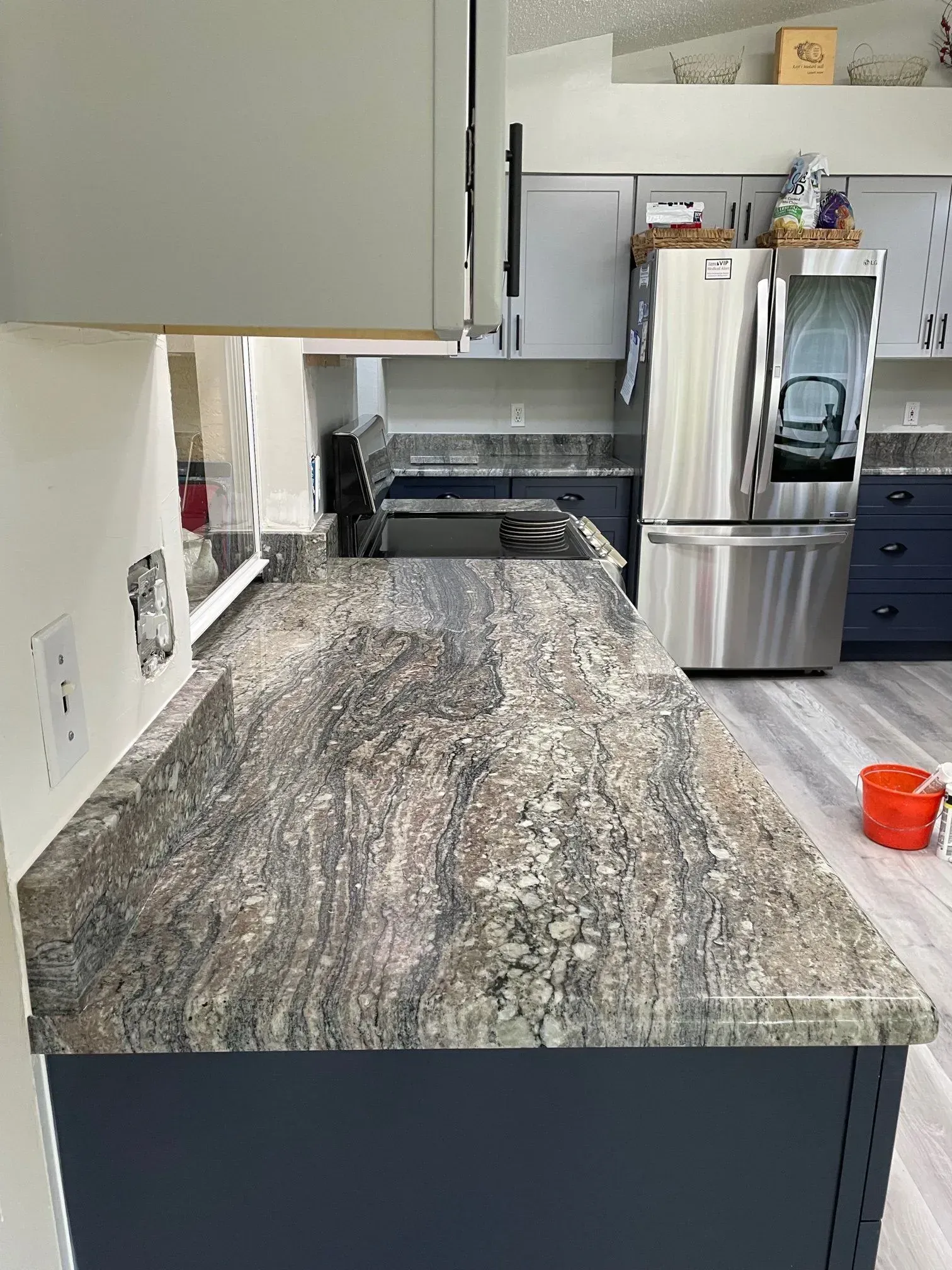 Kitchen with dark blue cabinets, granite countertops, and stainless steel refrigerator.
