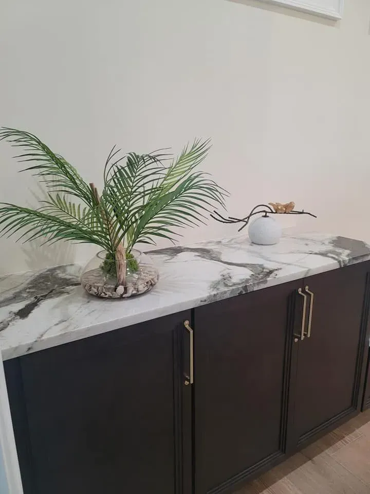 Dark brown cabinet with white marble countertop, a plant in a vase, and a small decorative item.