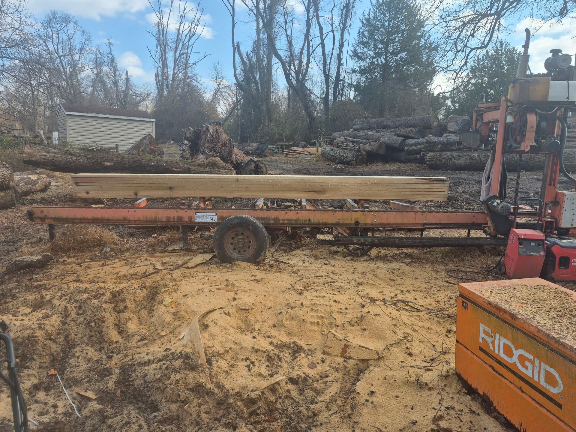 A portable sawmill cutting a log outdoors; sawdust covers the ground.