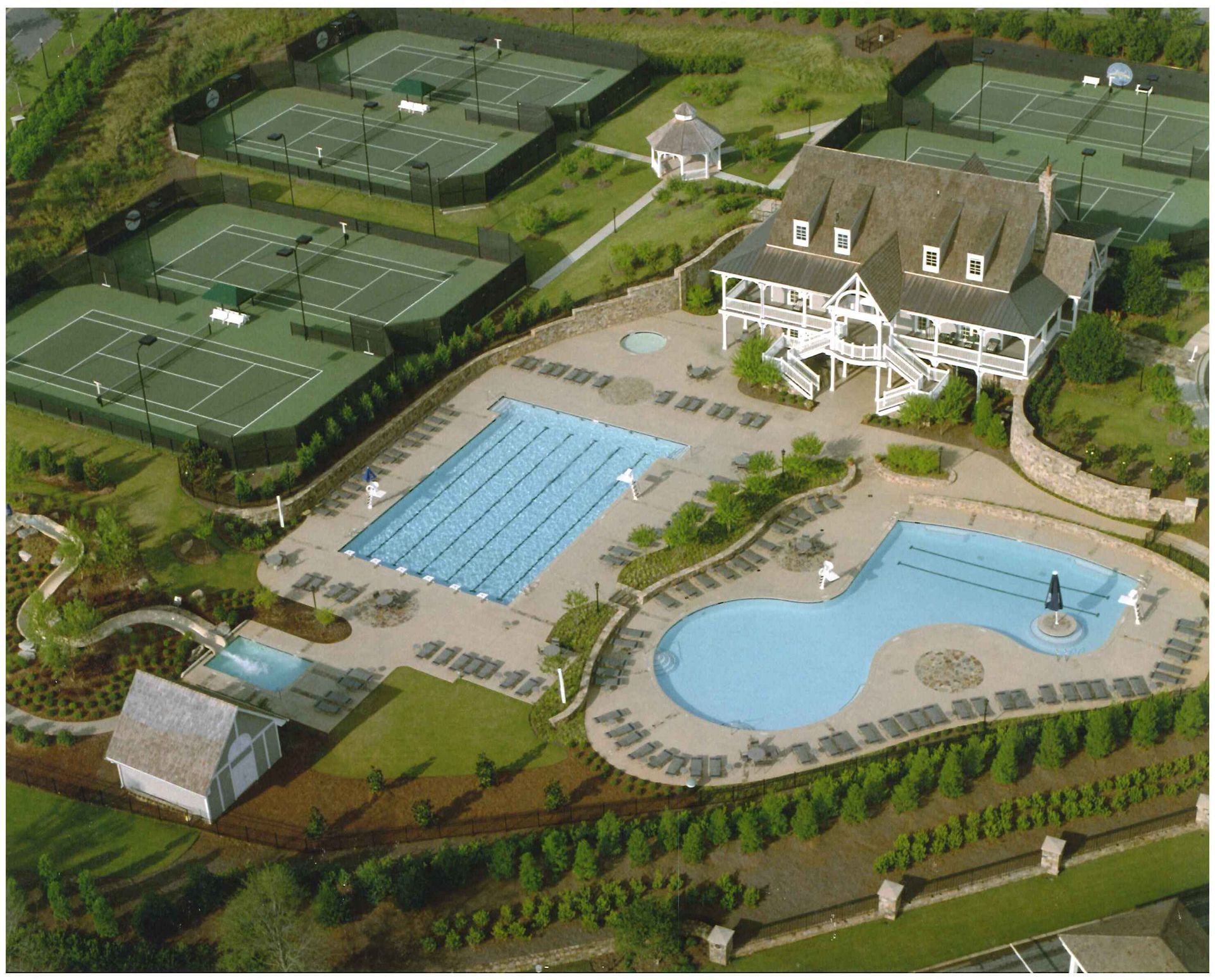 Aerial view of a recreational facility featuring several tennis courts, two outdoor swimming pools, and a clubhouse.