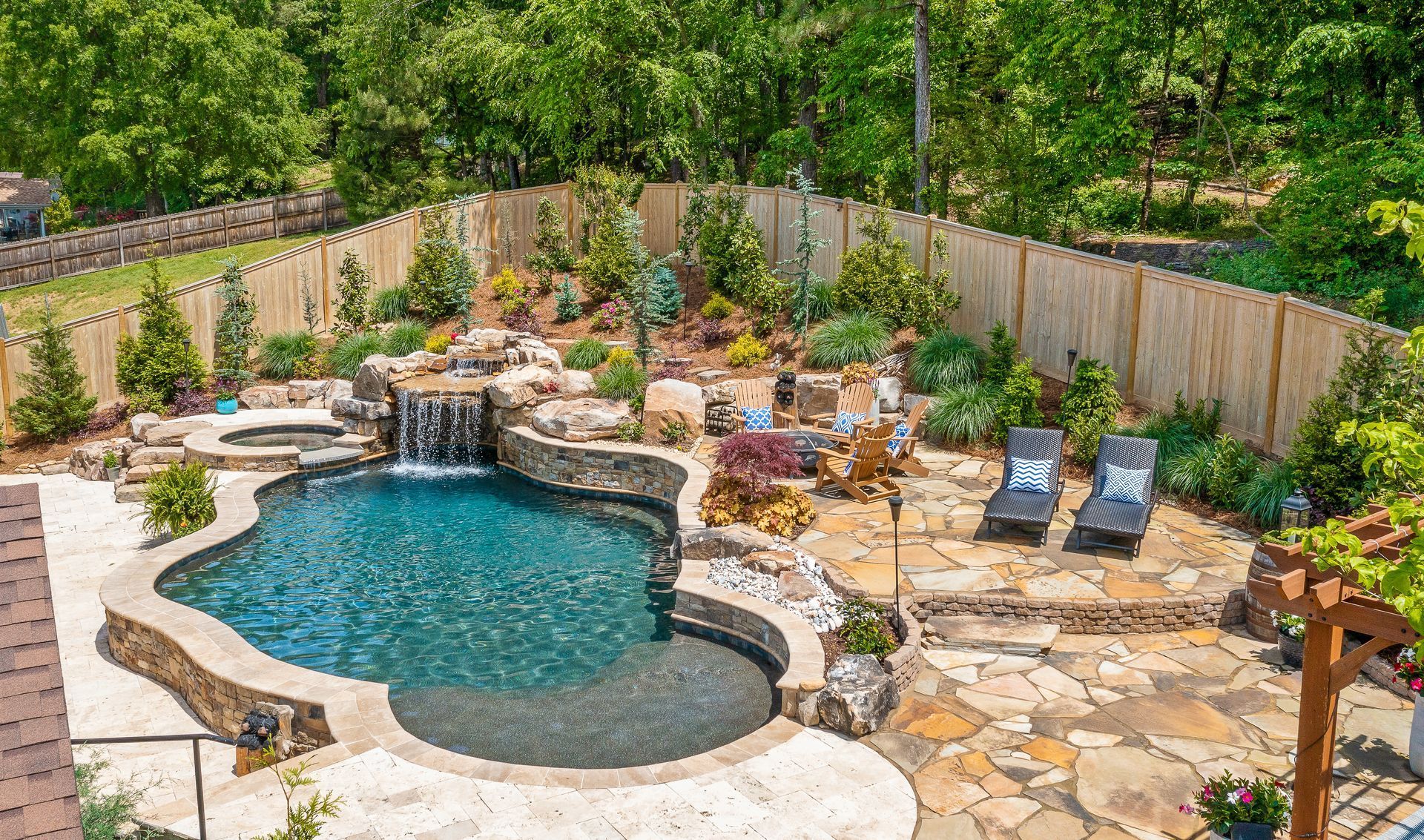 A high-angle view of a backyard featuring a freeform swimming pool with a stone waterfall, patio, and lounge chairs.
