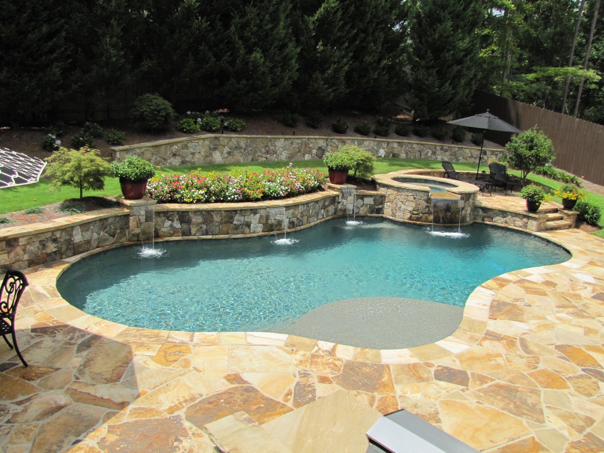 A kidney-shaped swimming pool with stone decking, a stone retaining wall, water features, and a small integrated spa.