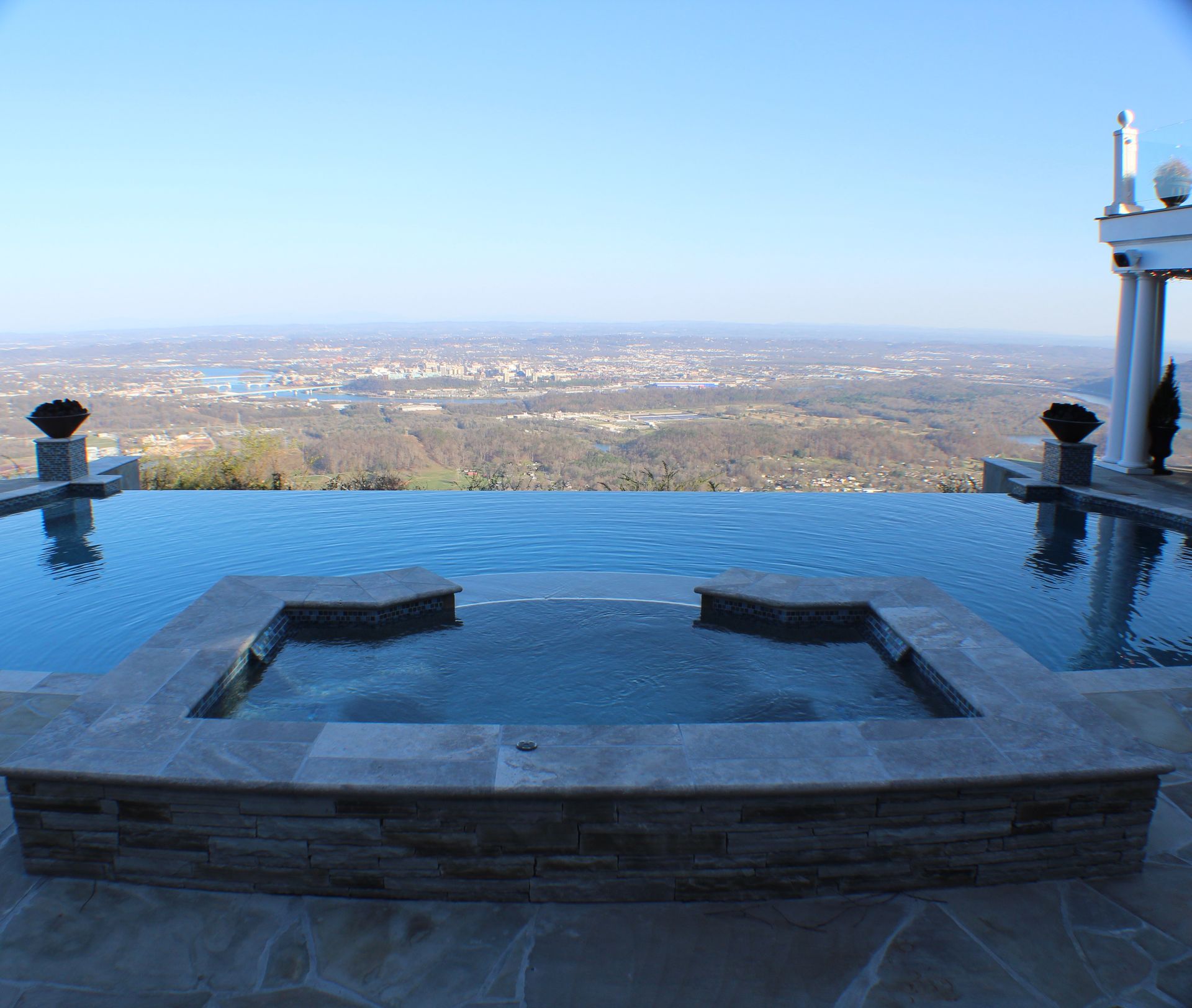 An infinity pool and spa overlooking a sprawling city landscape under a clear blue sky.