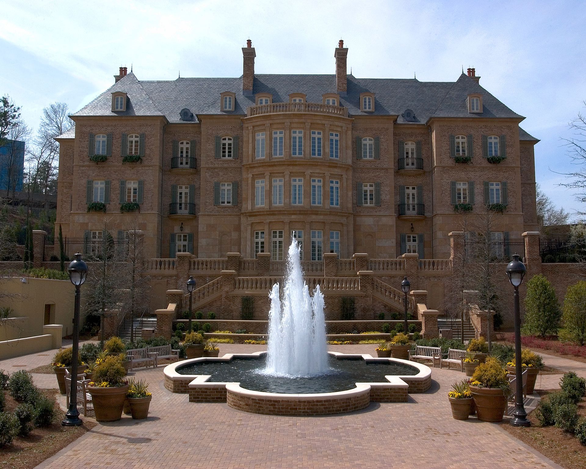 Large stone building with fountain in front; tiered garden, blue sky.