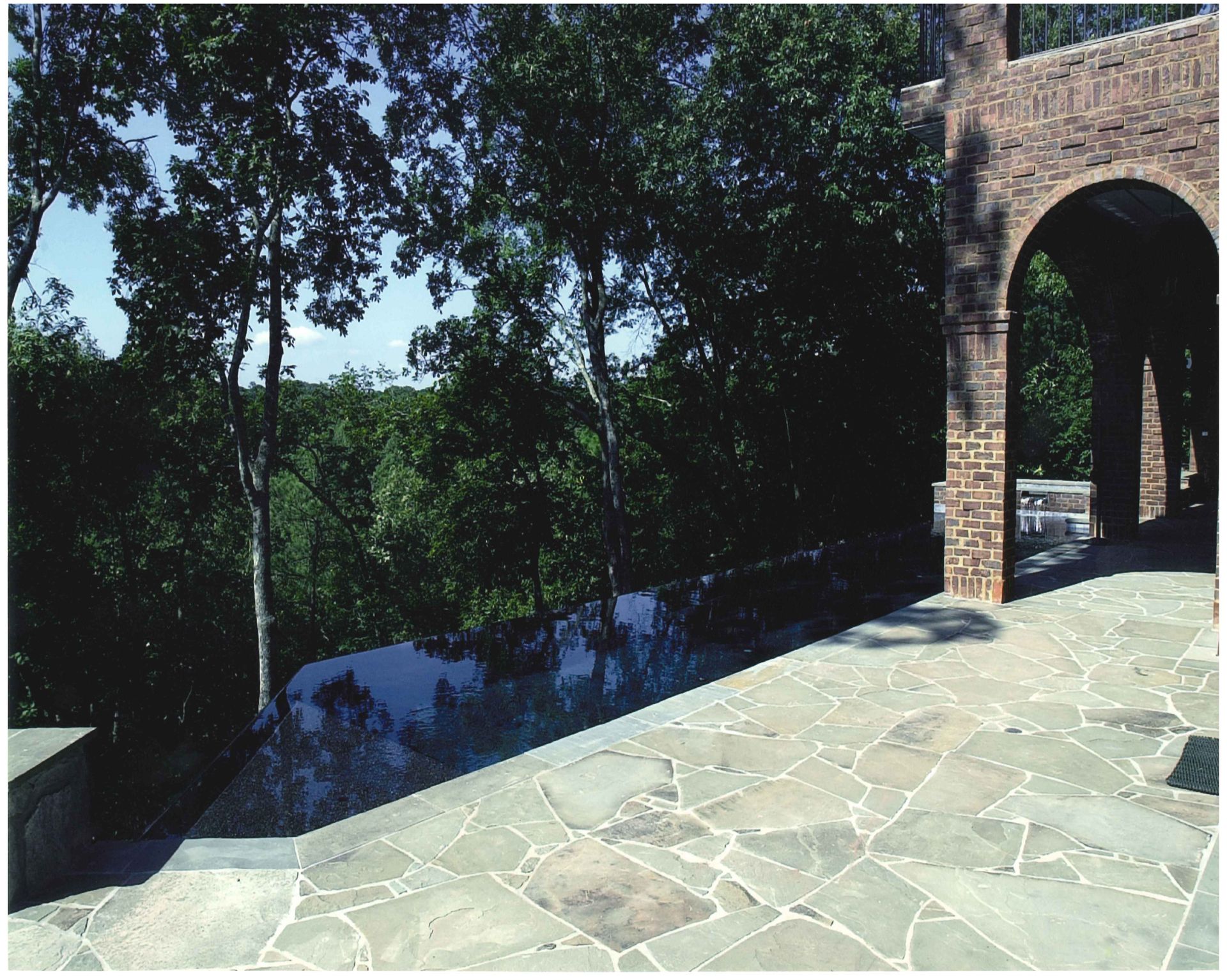 Stone patio with reflective pool, trees, and arched brick structure.