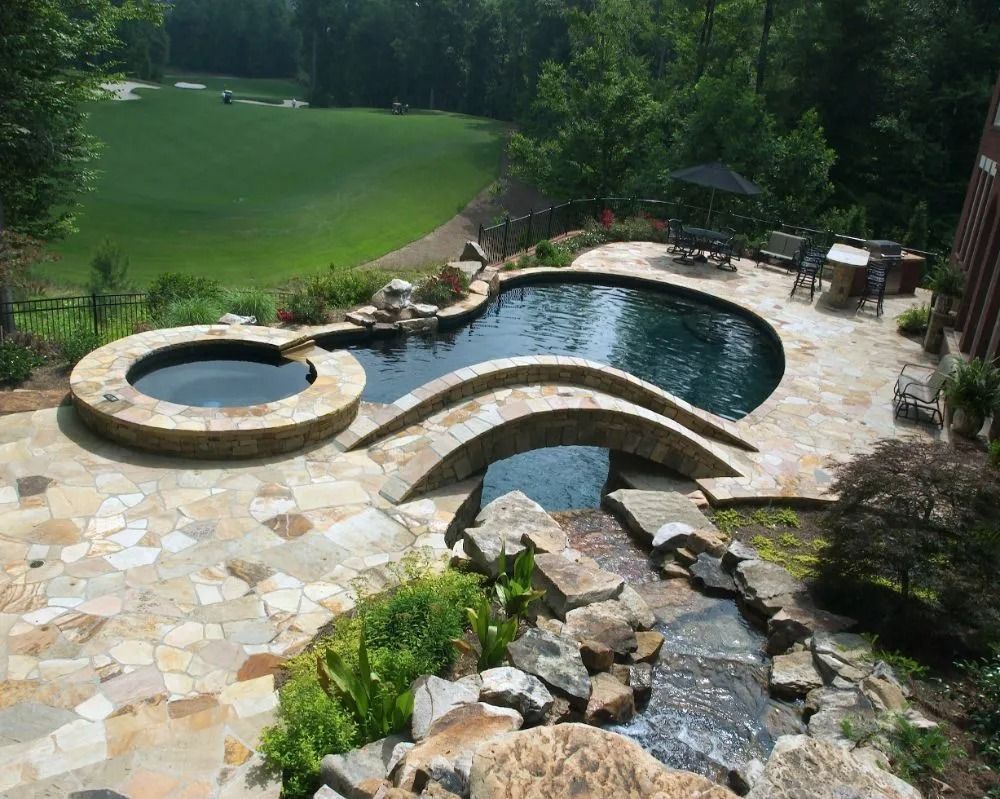 Stone patio with pool, hot tub, and waterfall overlooking a golf course.