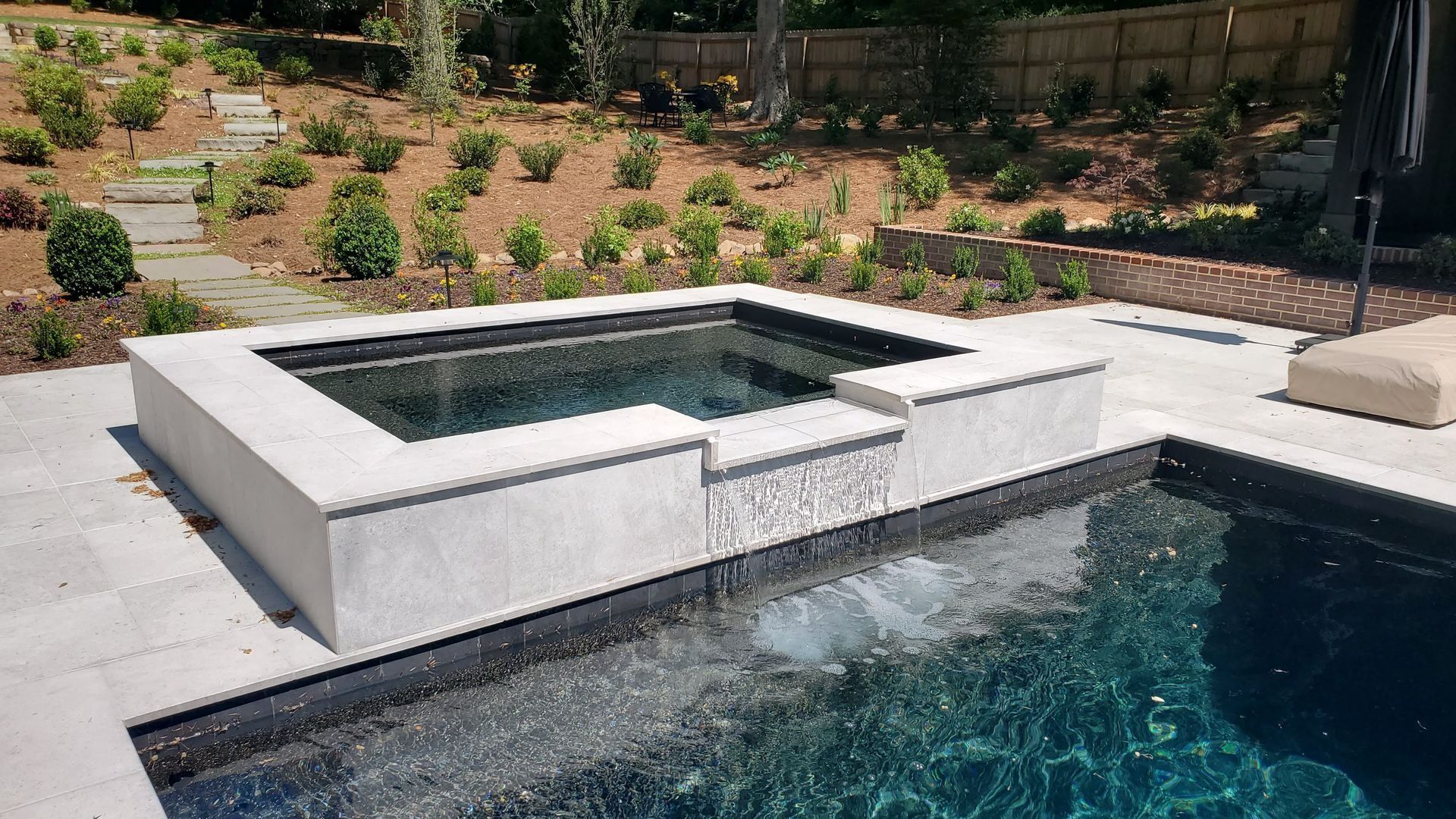 Hot tub integrated into a pool with a cascading waterfall feature in an outdoor setting.