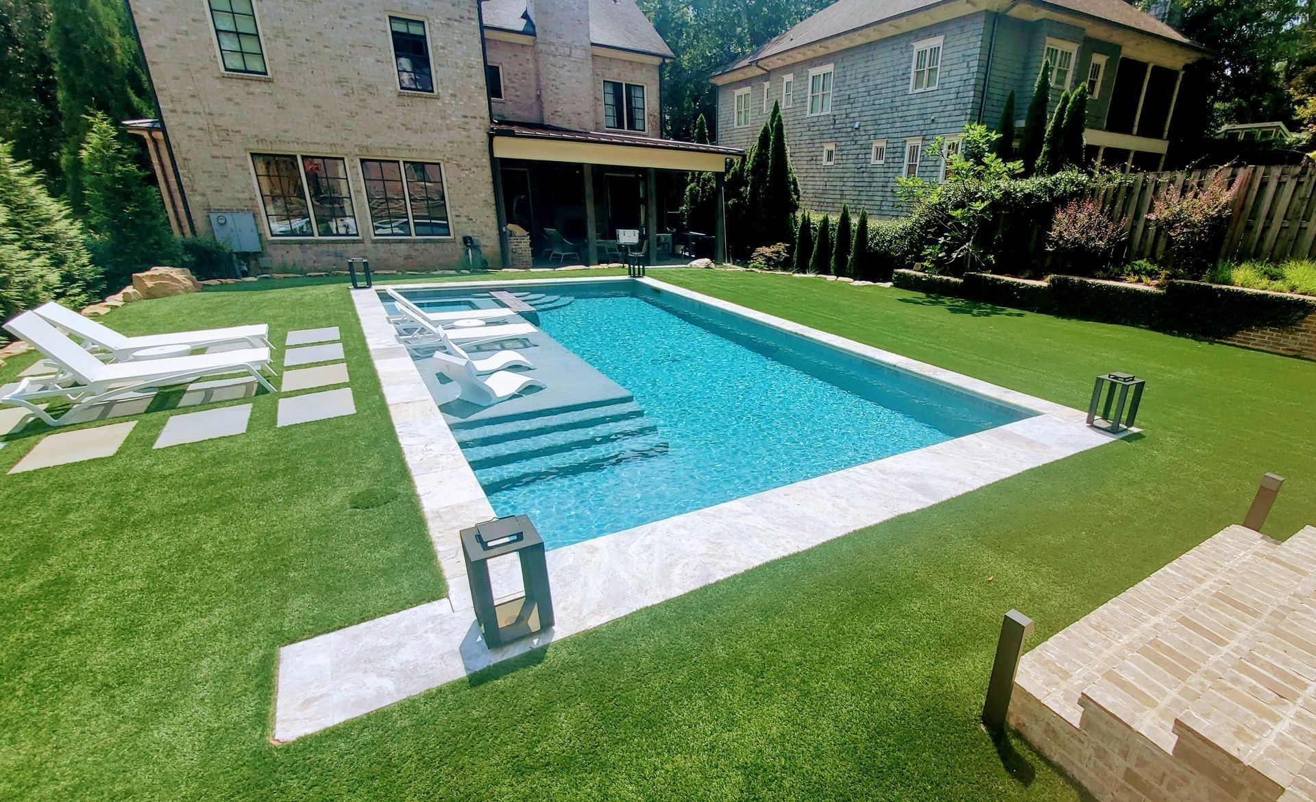 Backyard with a rectangular swimming pool, surrounded by green grass. Houses visible in background.