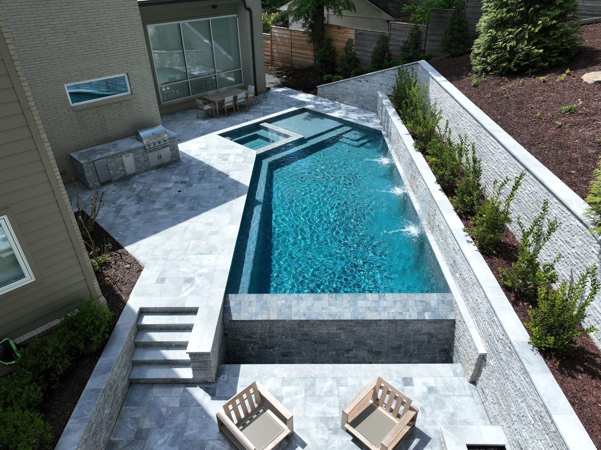 Modern backyard with a turquoise pool, hot tub, patio, and stone walls.