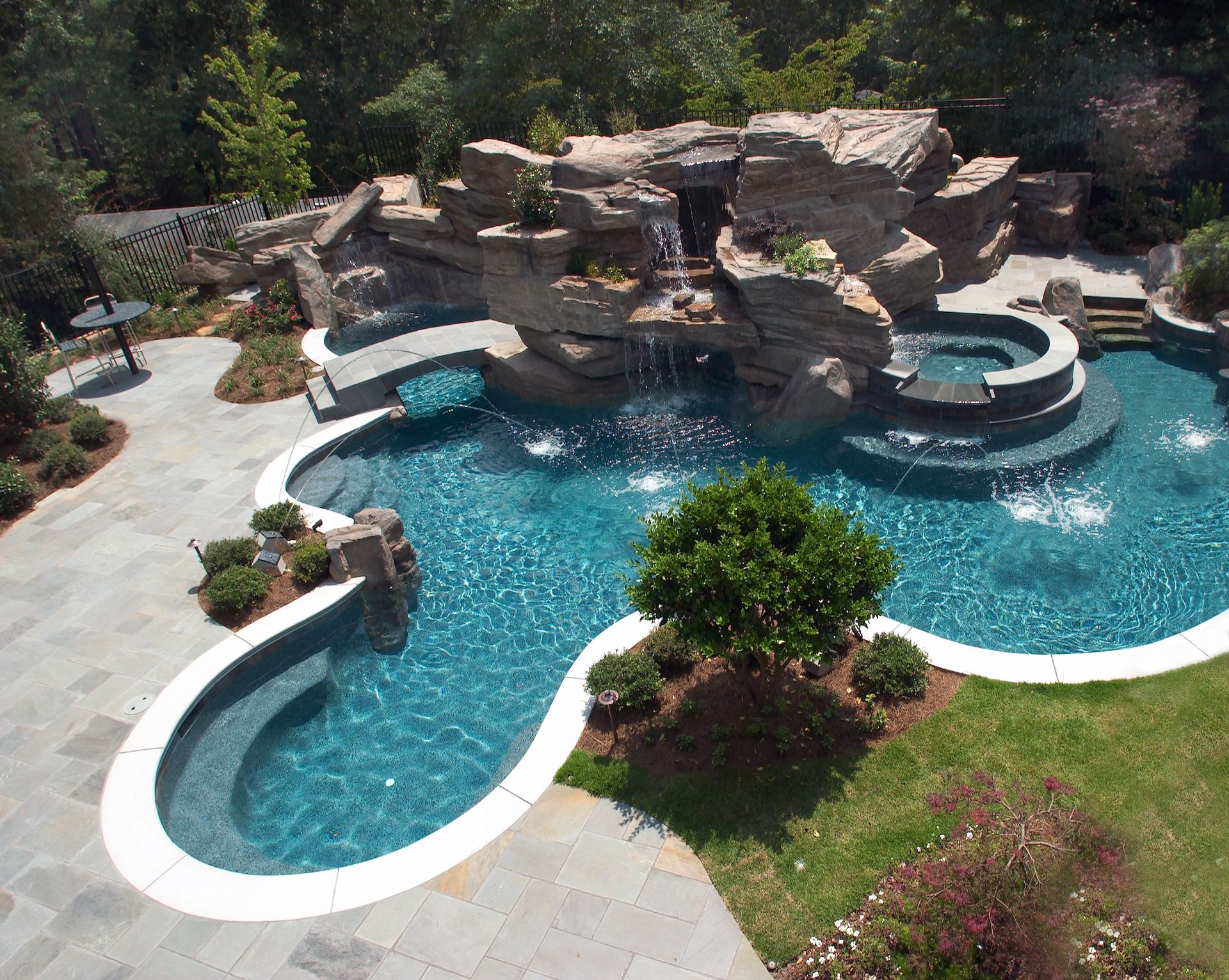 Luxury swimming pool with waterfall feature and hot tub. Blue water, stone accents, and surrounding landscaping.