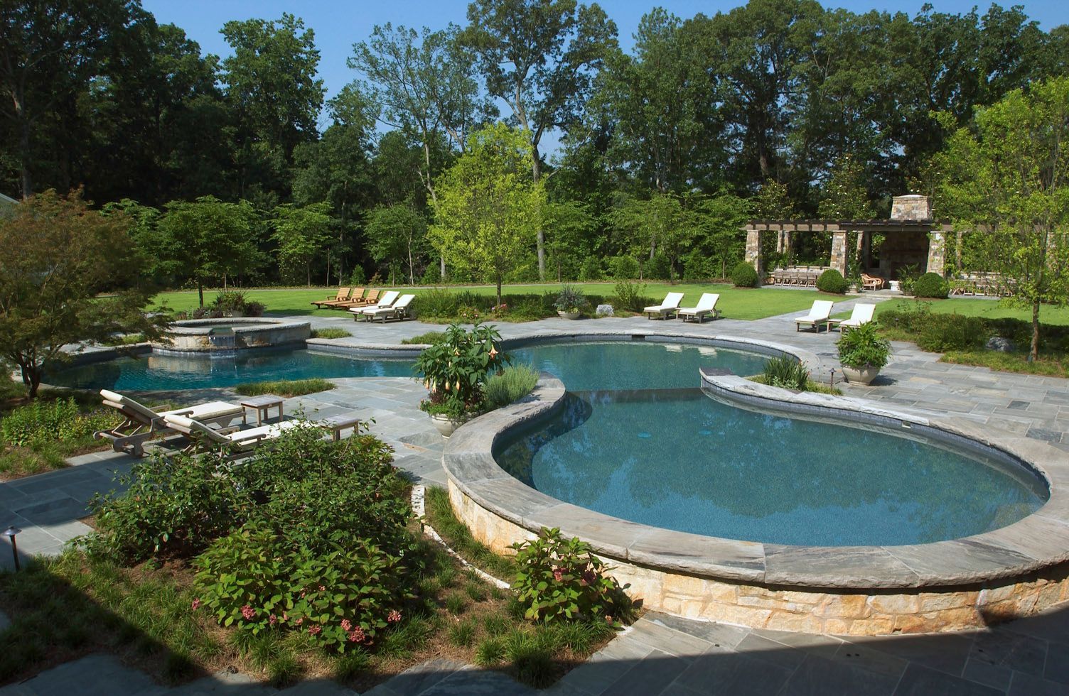 Large outdoor pool with stone border, surrounded by lush landscaping and trees.