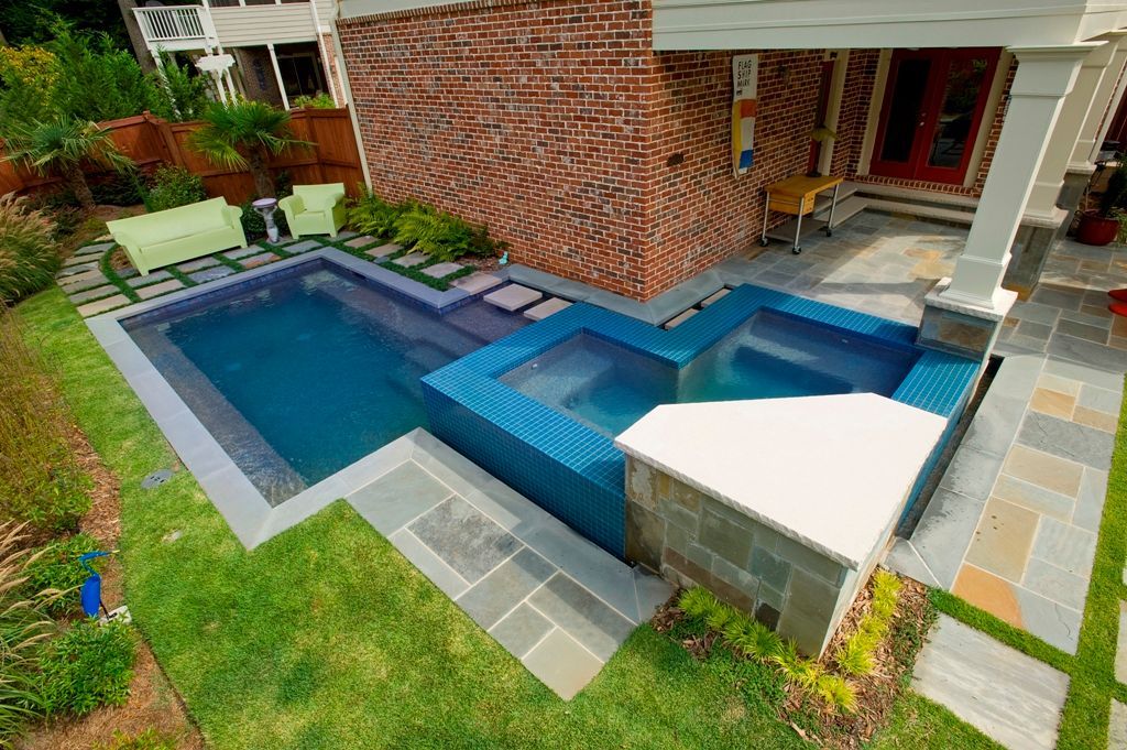 Outdoor pool and spa with brick wall, lawn, and patio, in a residential setting.