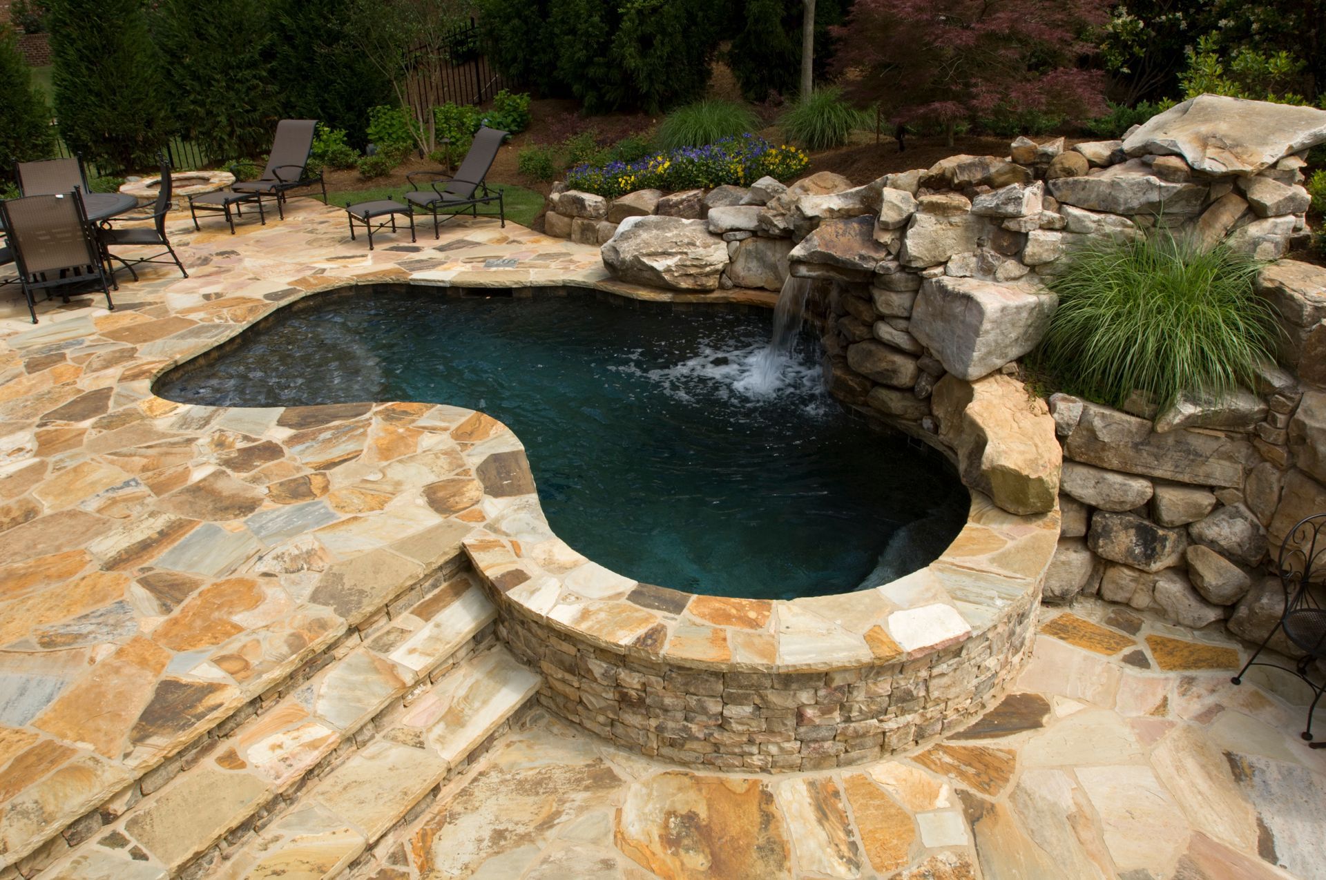A natural stone pool and waterfall set in a landscaped patio area with outdoor seating.