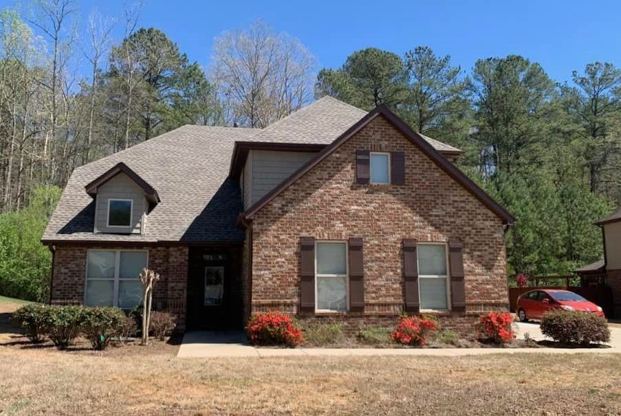 Brick house with brown shutters, a small dormer, and a red car in the driveway on a sunny day.