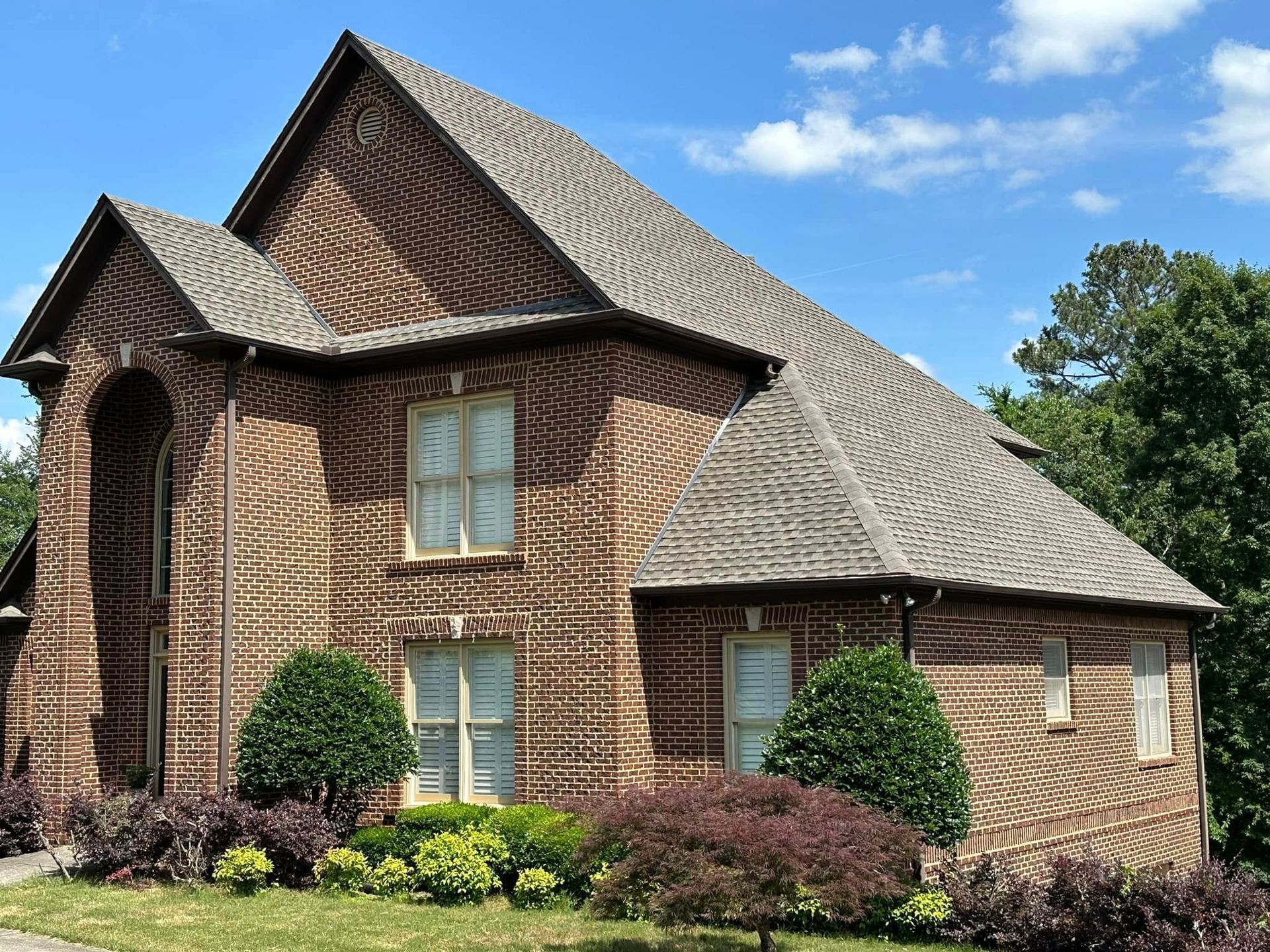 Brick house with multiple gables and windows, surrounded by landscaping, under a blue sky.