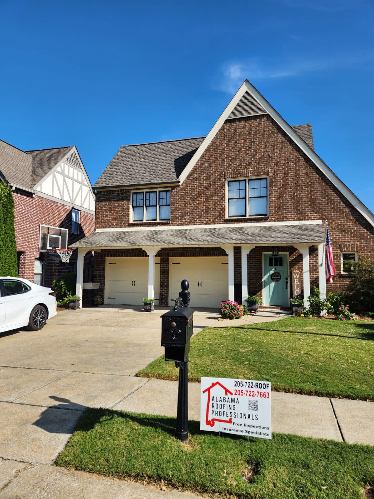 Brick house with two-car garage, white trim, and light blue door. Sign in yard. Sunny day.