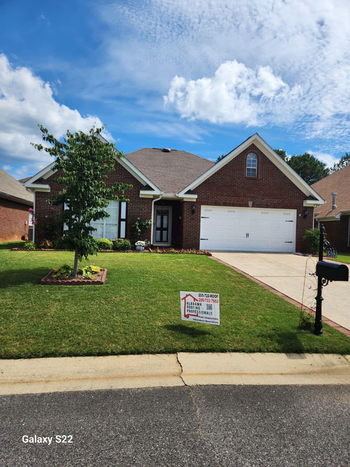 A brick house with a white garage door, well-manicured lawn, and blue sky.