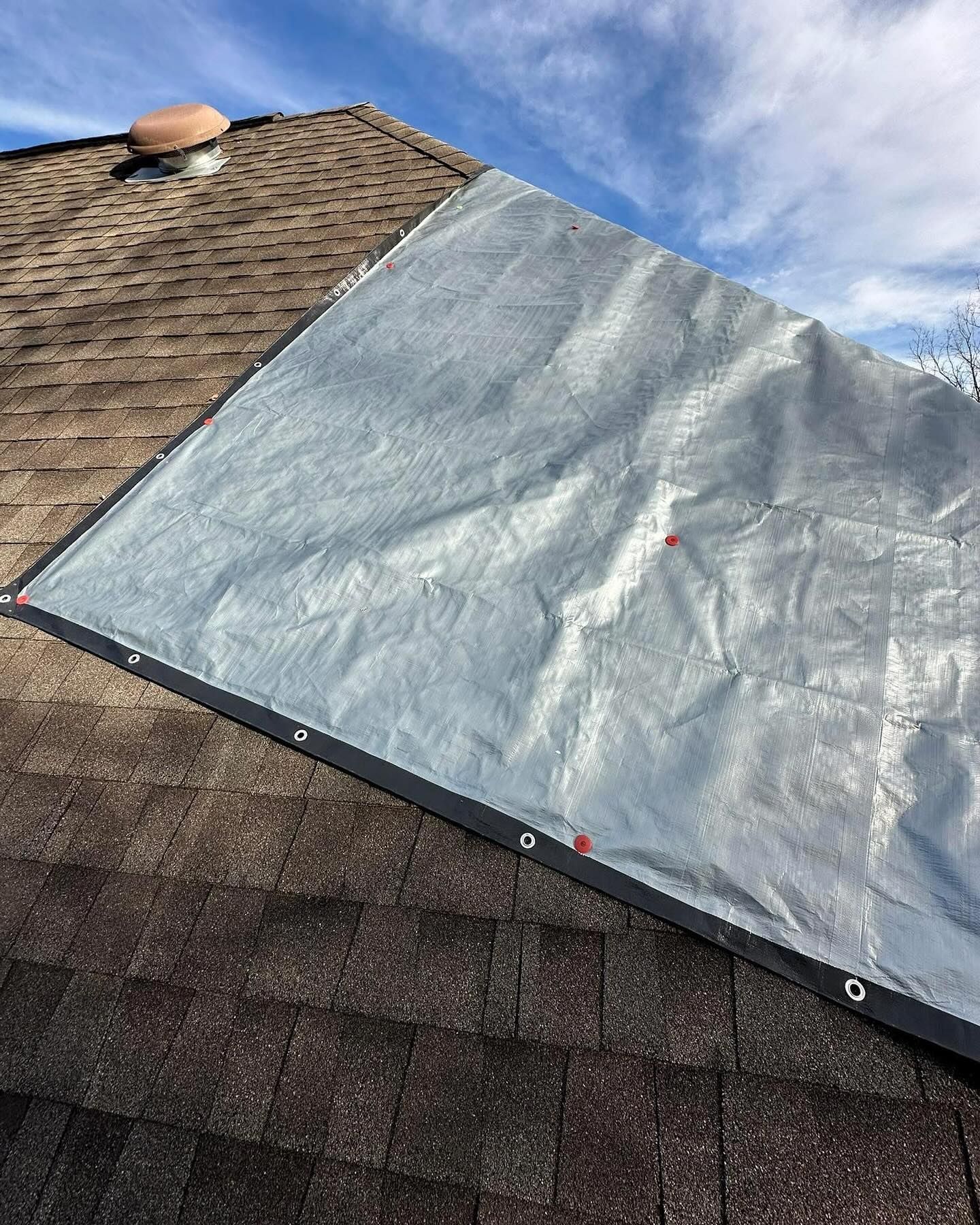 Silver tarp covering part of a brown shingled roof, protecting it from the elements.