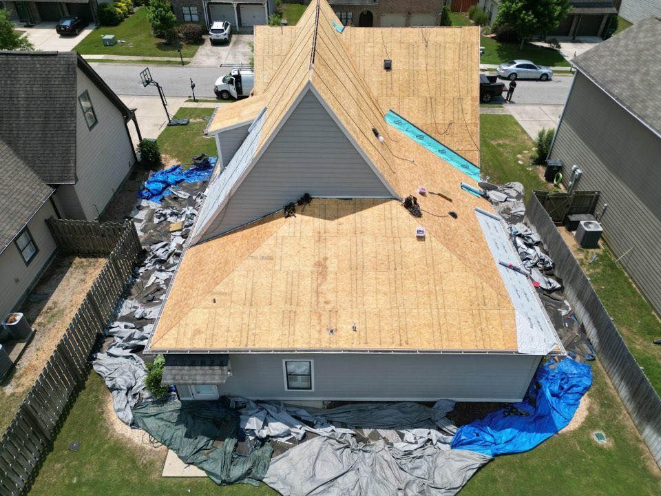 House with roof being repaired; blue tarps cover the lawn; workers visible.