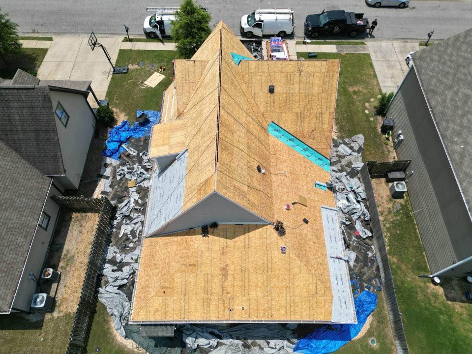 Aerial view of a house roof undergoing repair; sections of shingles removed, blue tarps cover ground.