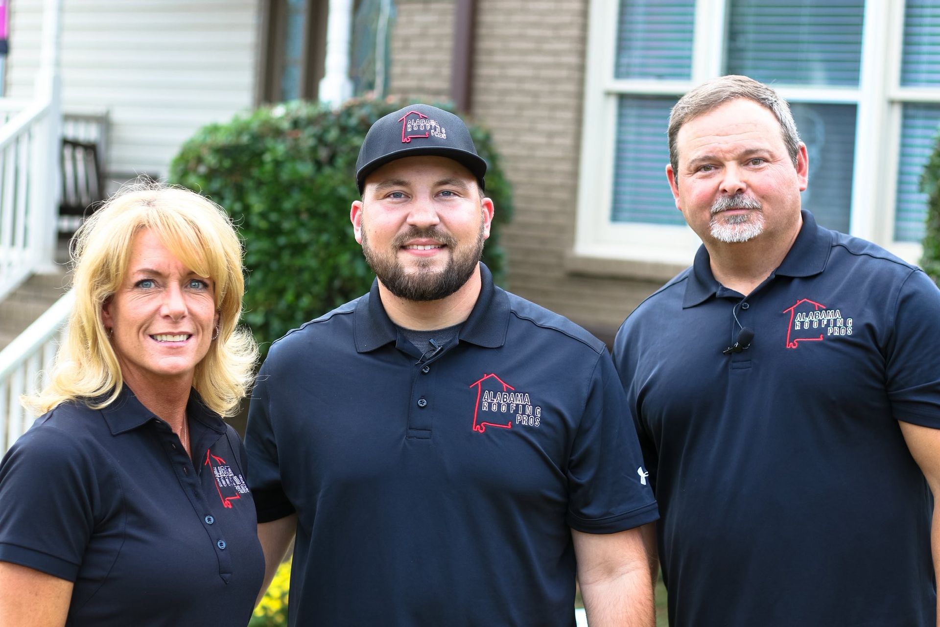Three people in black shirts with a company logo in front of a house.