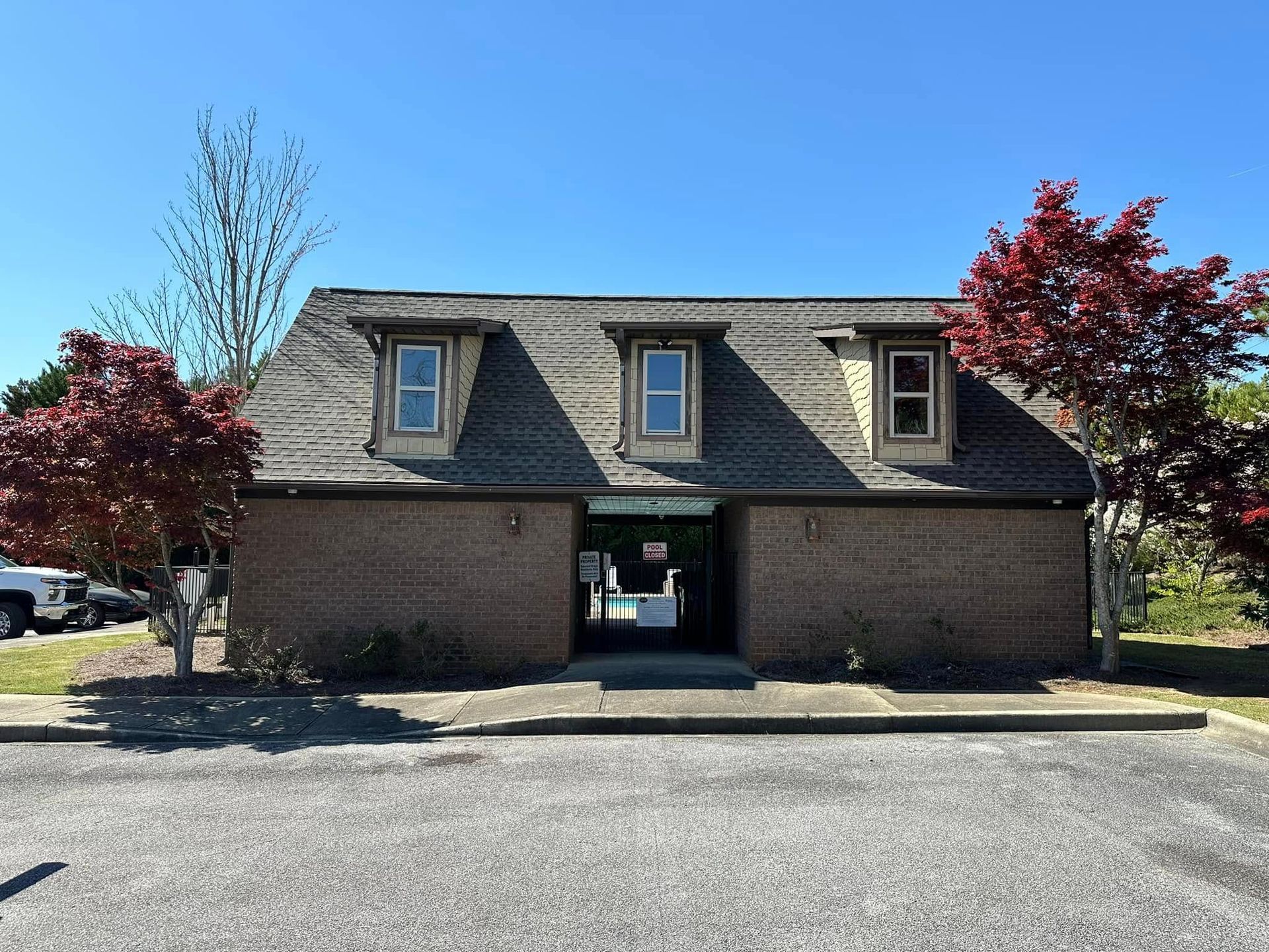 Brick building with three dormer windows, surrounded by red trees, clear blue sky.