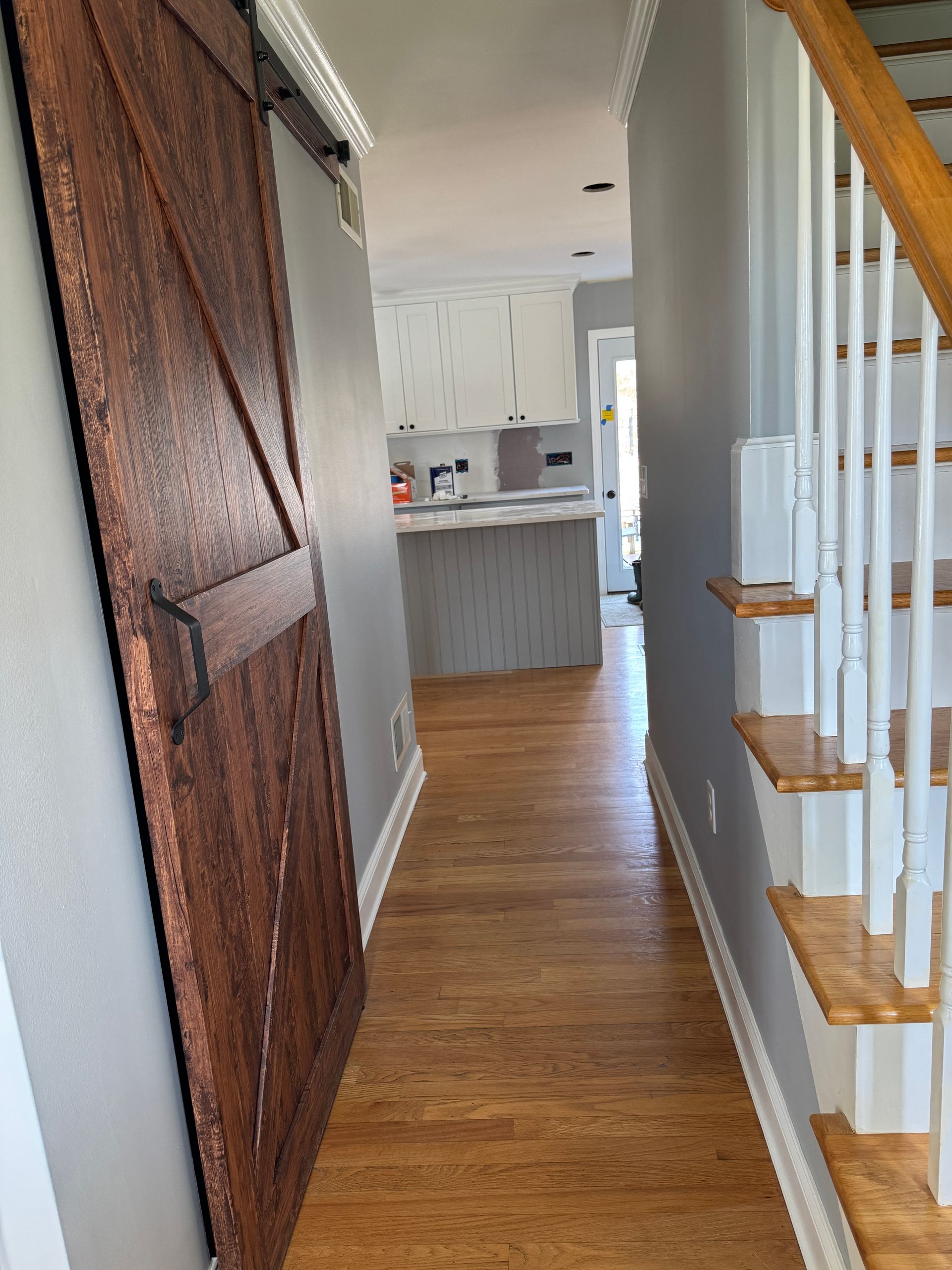 Narrow hallway with wood floor, barn-style door, and staircase leading to a small kitchen.