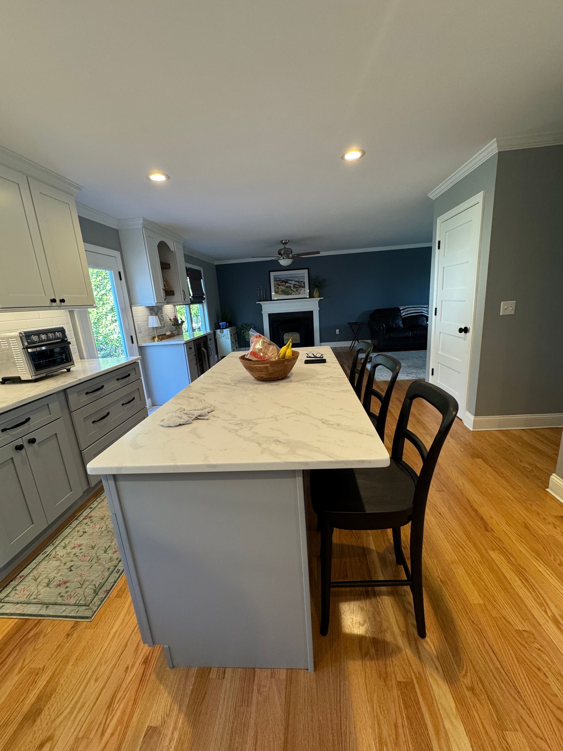 Modern kitchen with white island, black barstools, hardwood floors, and a living room in the background