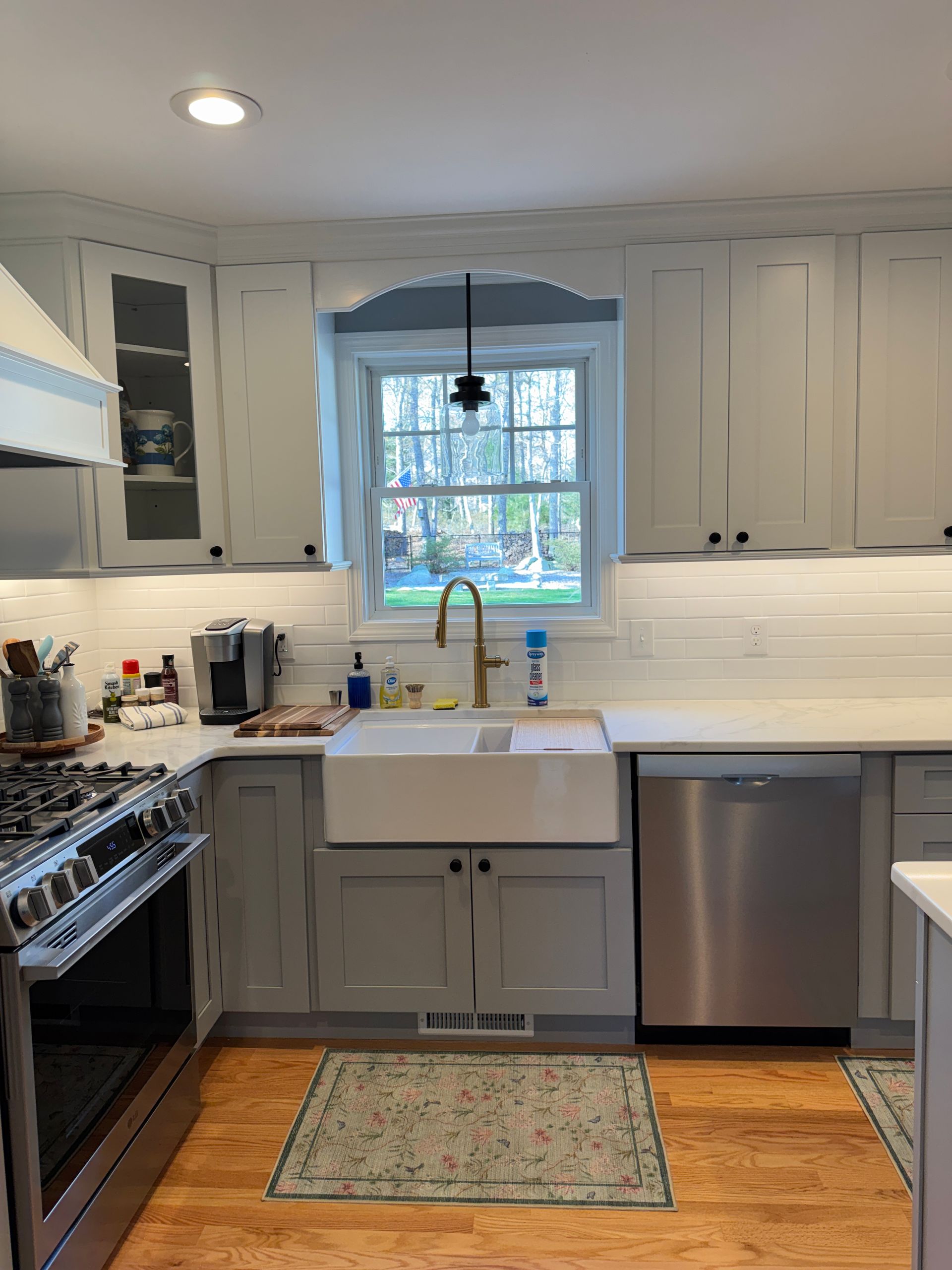 Bright kitchen with white cabinets, farmhouse sink, stainless dishwasher, gas range, and a window above the sink.