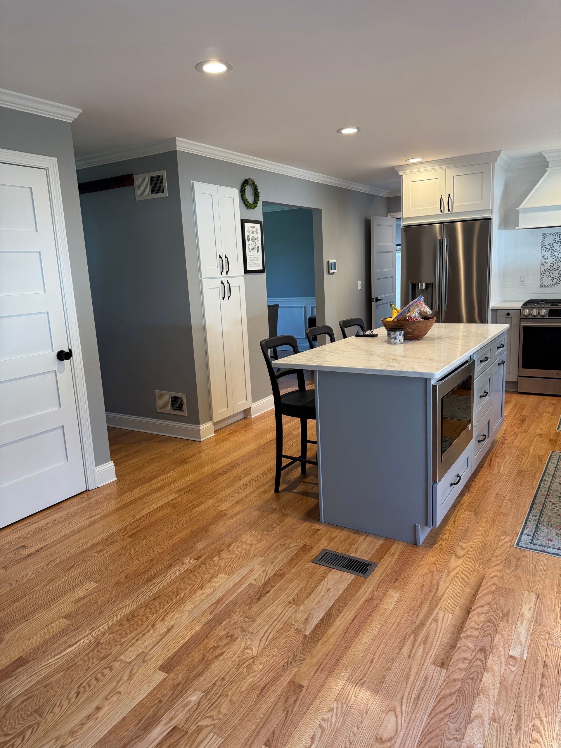 Bright modern kitchen with island, stainless fridge, gray walls, and hardwood floors.