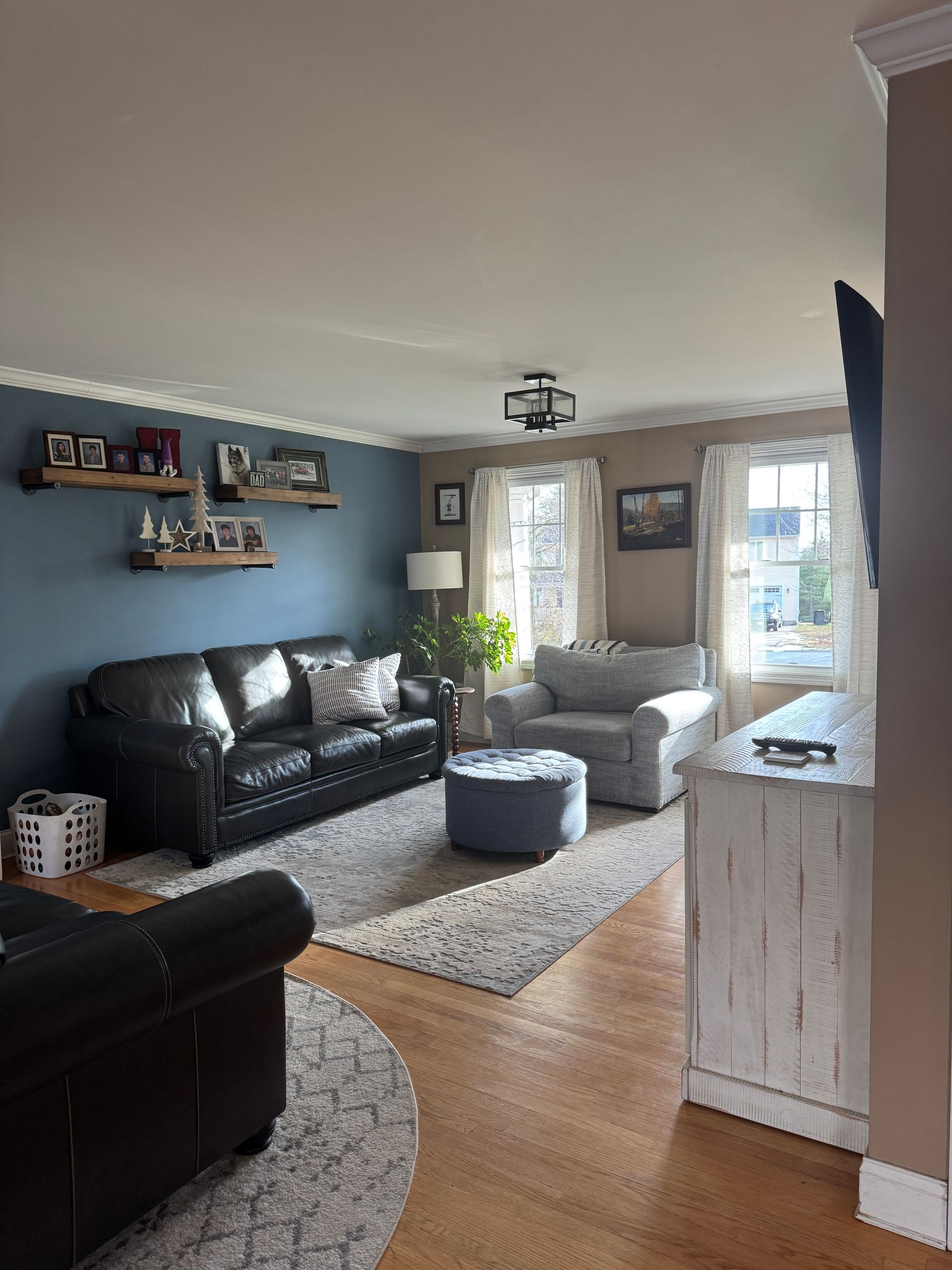 Bright living room with black and gray sofas, light wood floors, and a windowed seating area.