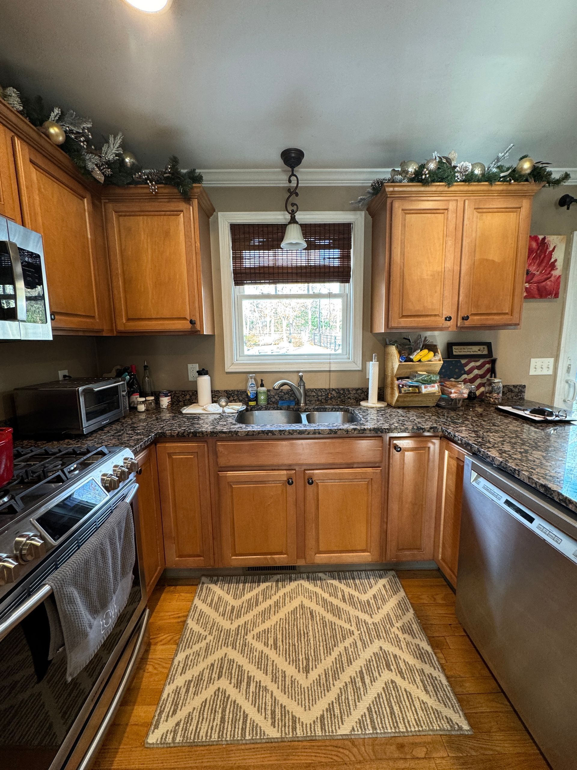 Small kitchen with wooden cabinets, granite counters, stainless appliances, and a window over the sink.