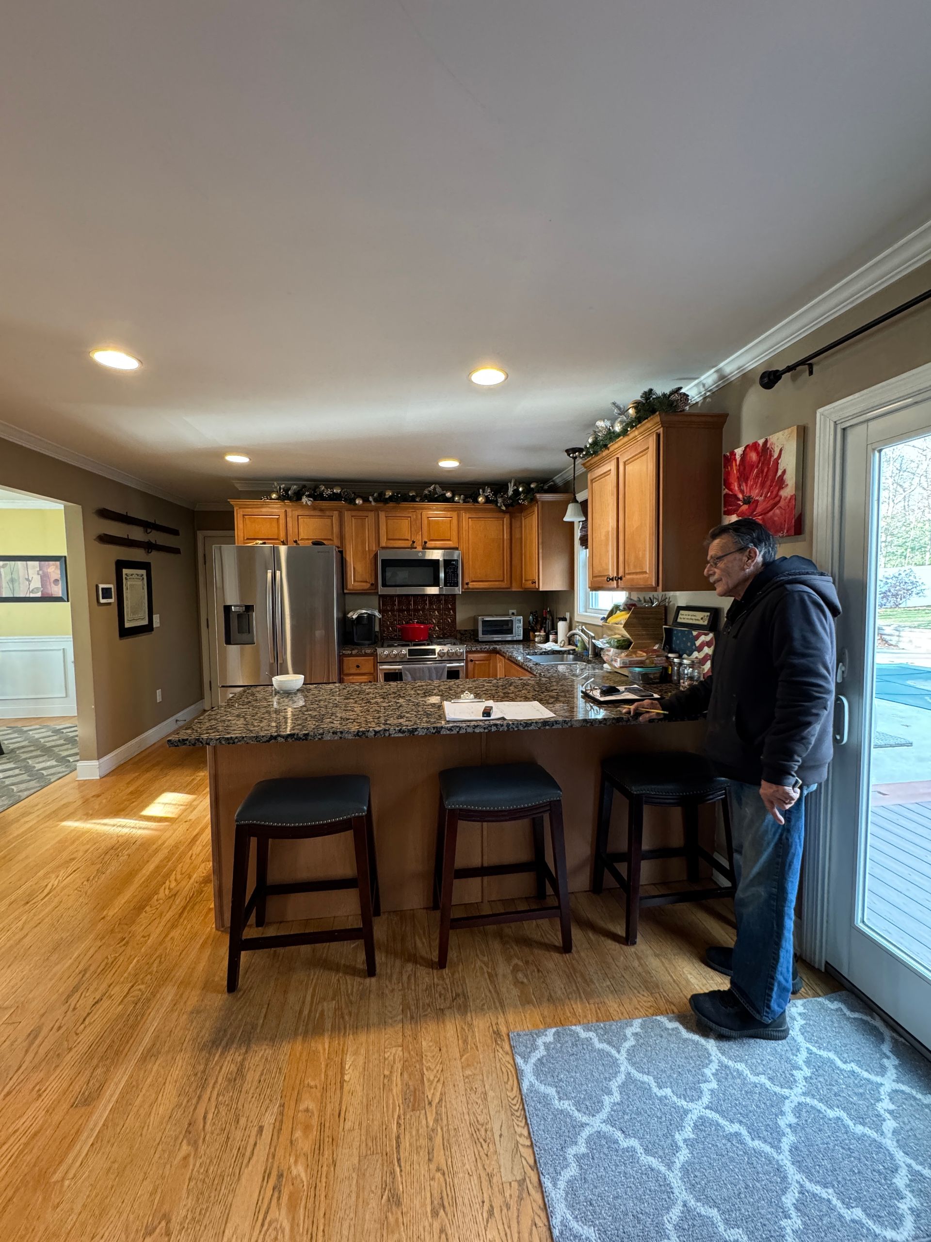 Kitchen with wood cabinets and granite island, with a person standing by the counter near sliding glass doors.