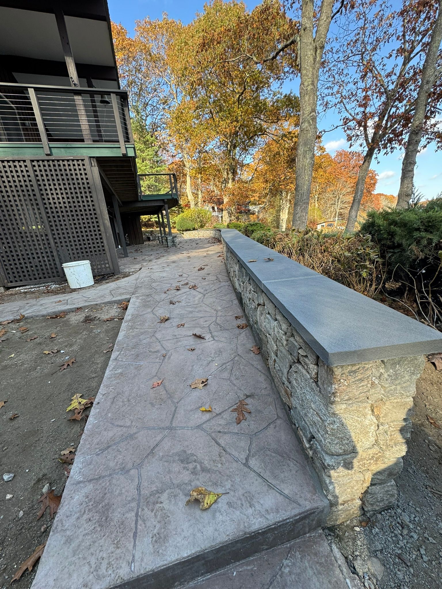 Concrete ramp beside building, leading through an outdoor area with autumn trees and fallen leaves.