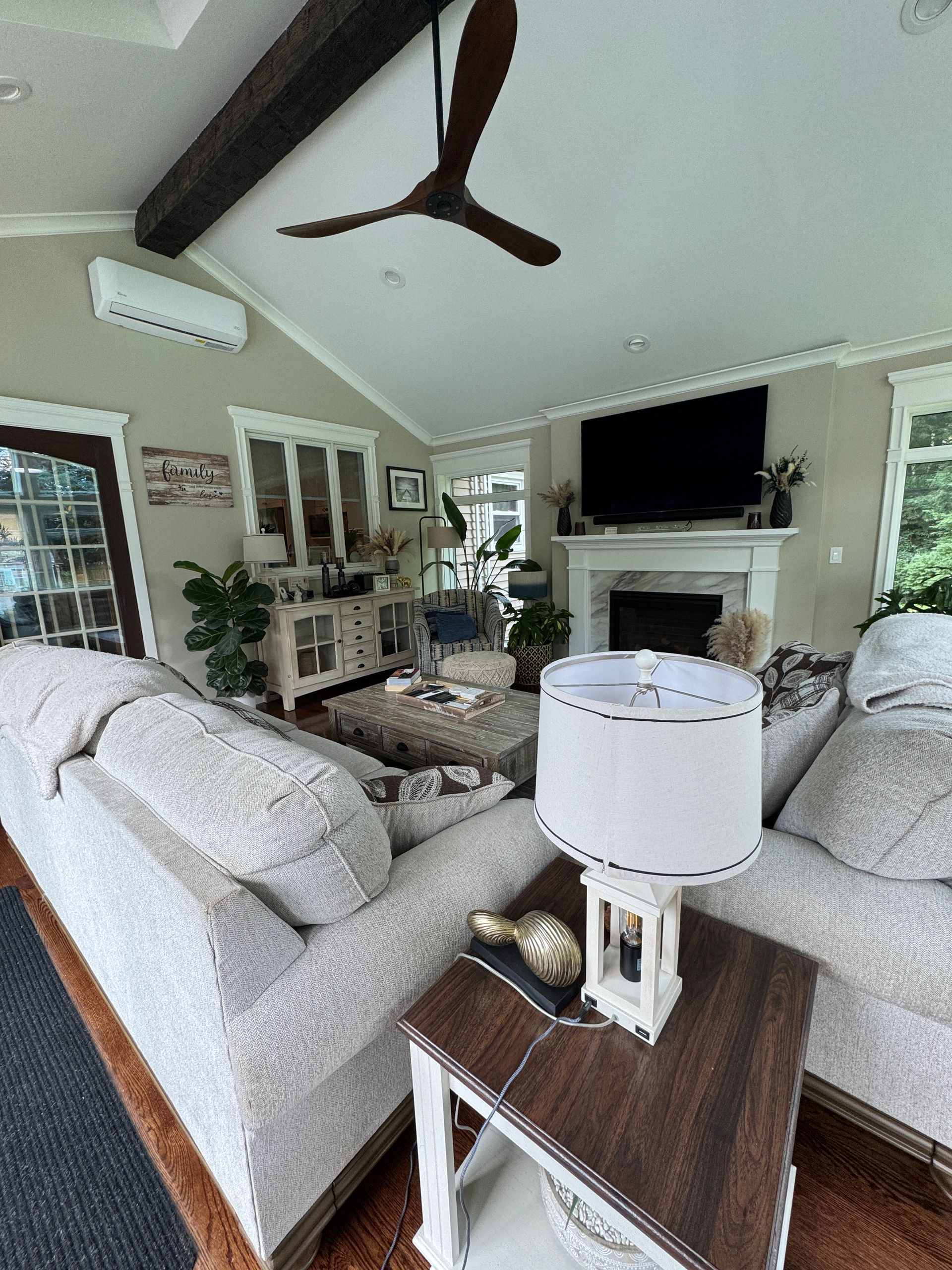 Bright living room with gray sofas, a fireplace, wall TV, and vaulted ceiling with a ceiling fan.