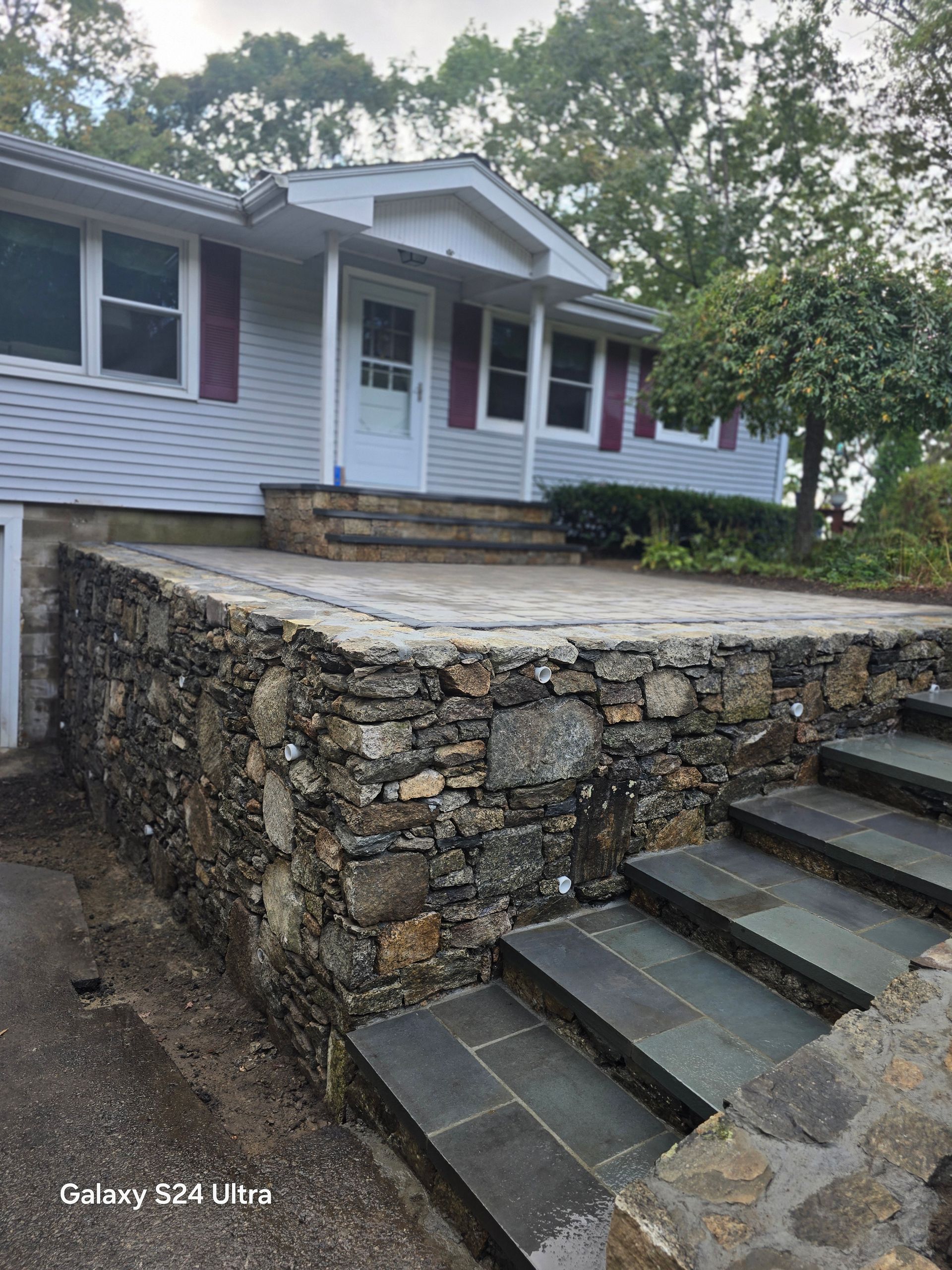 Front porch of a white house with a stone retaining wall and concrete steps up to the entrance
