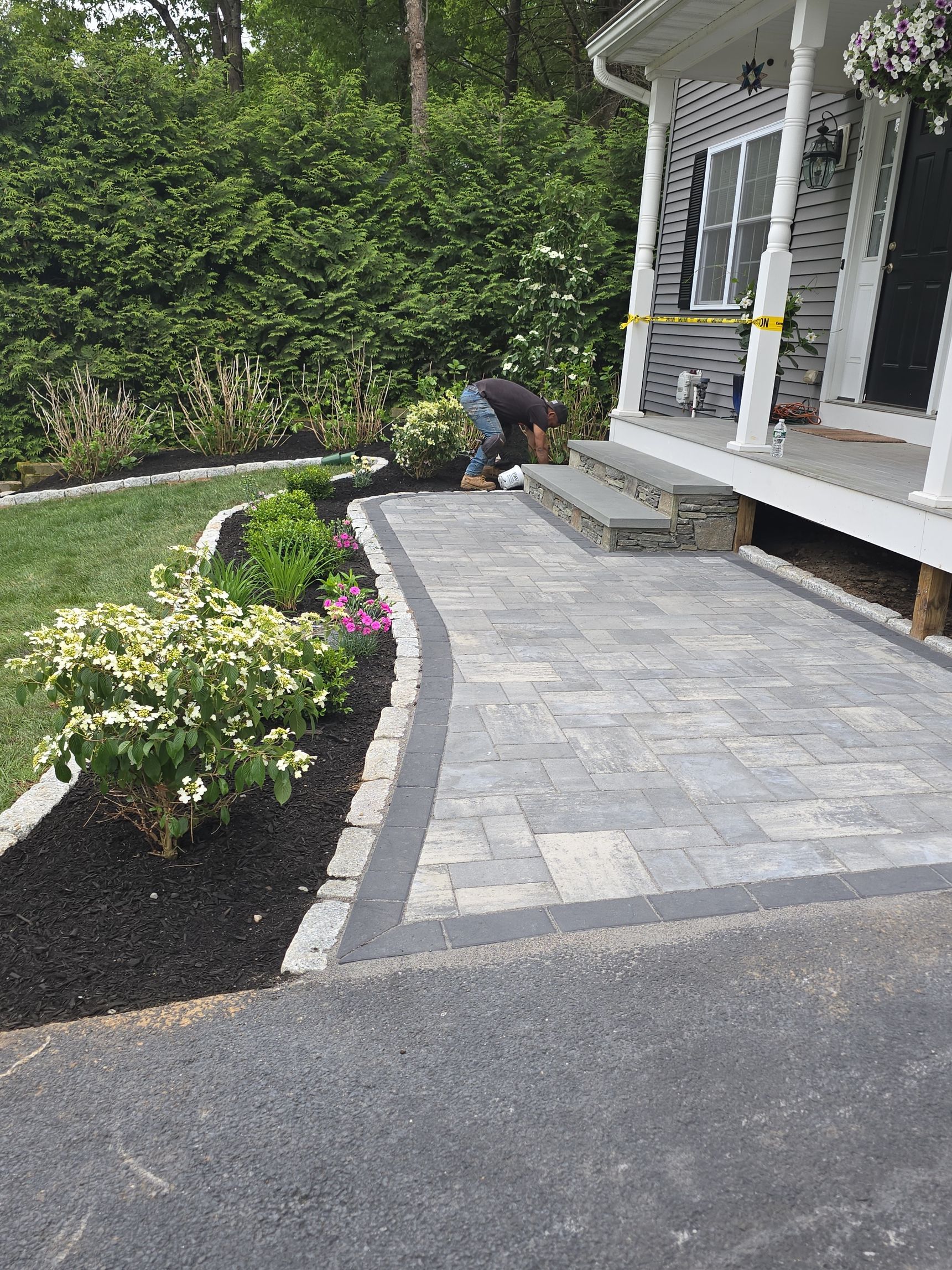 Brick walkway leading to a porch with steps, bordered by shrubs and garden beds