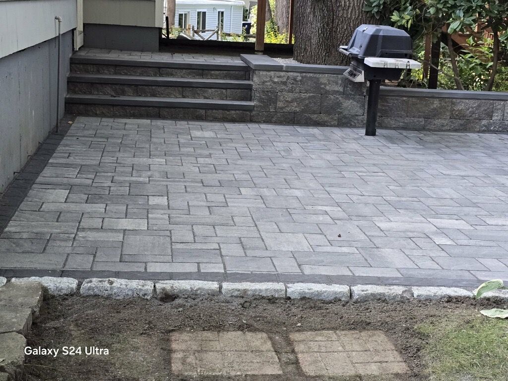 Stone patio and steps leading to a driveway, with a black grill on the right.