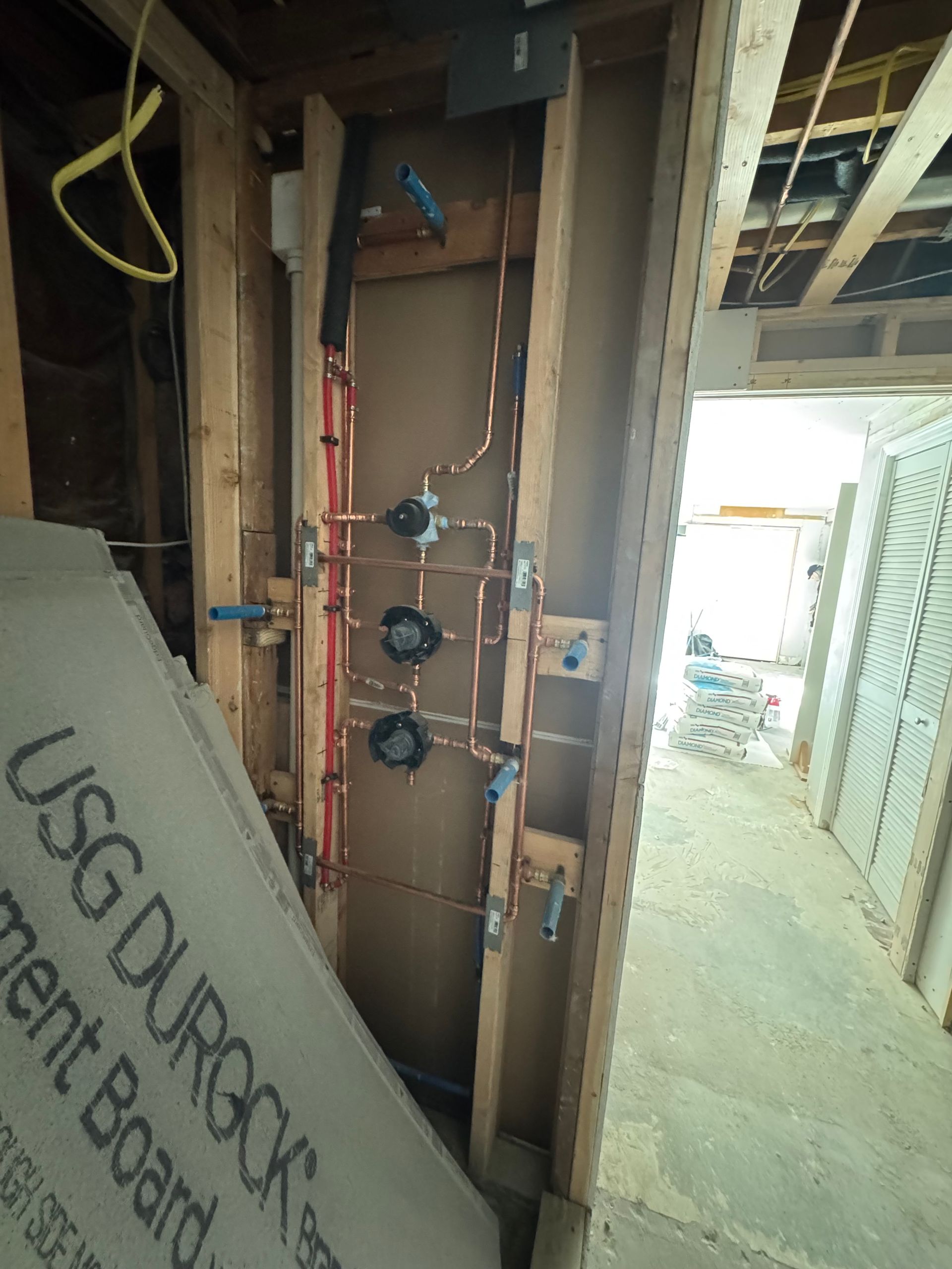 Exposed plumbing and electrical in a construction site hallway, with insulation boards leaning against the wall.