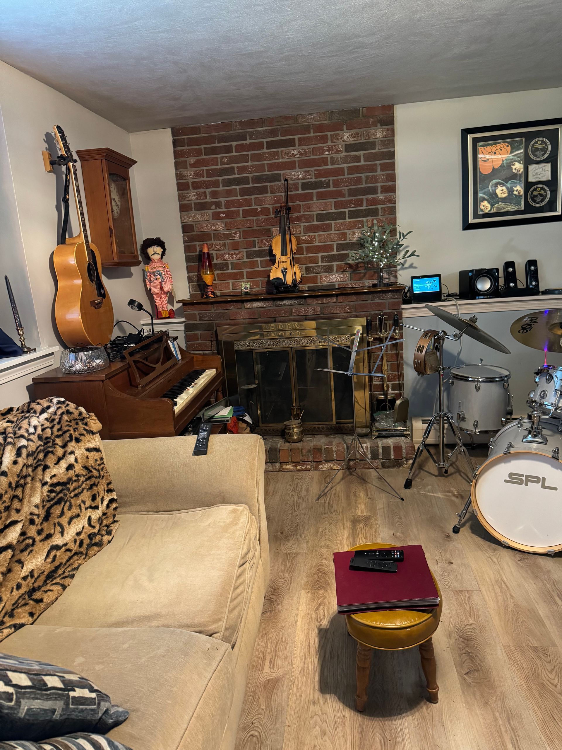 Living room music studio with guitars, drum kit, piano, and brick fireplace