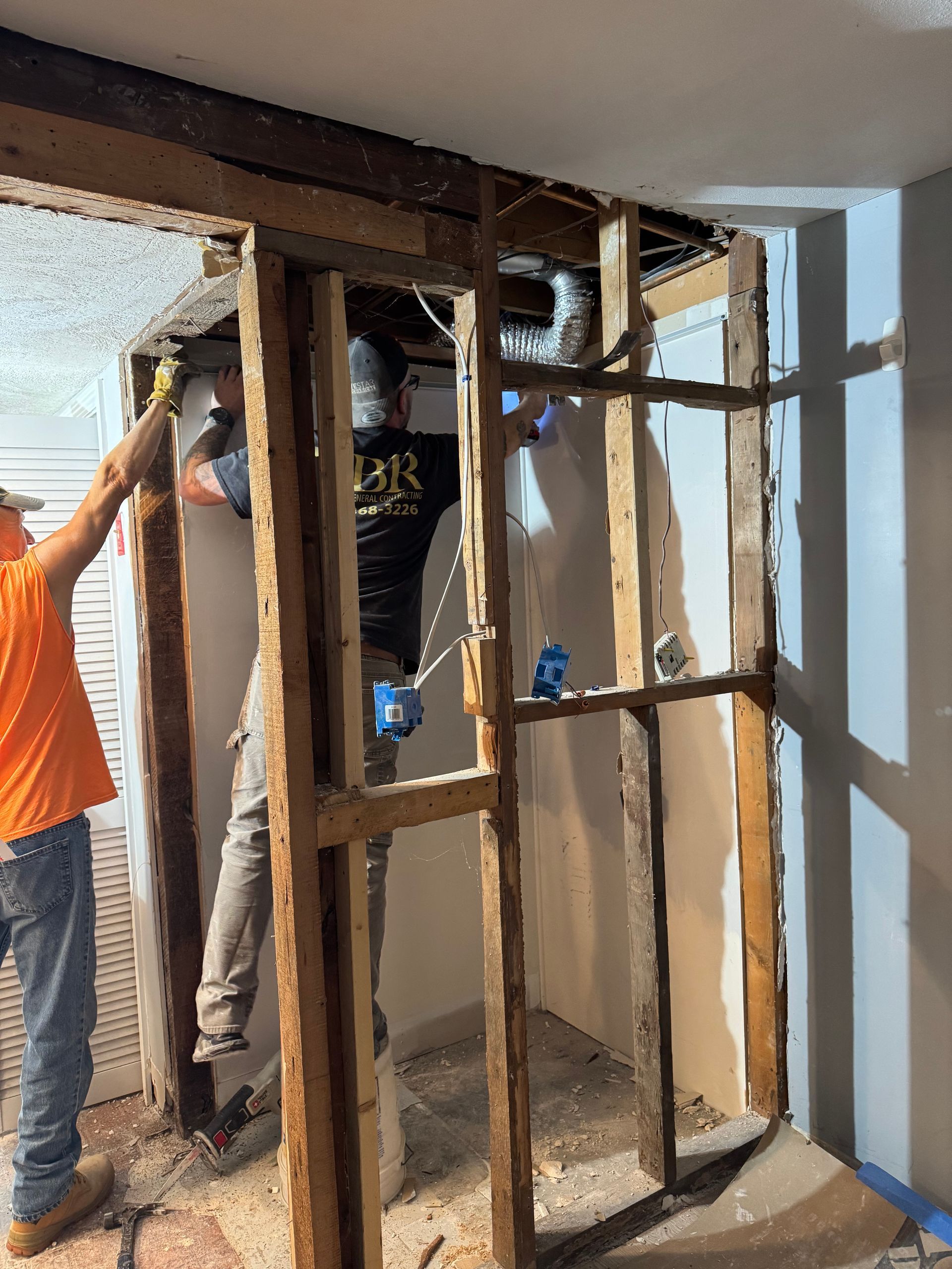 Workers removing an interior wall with exposed studs and debris during renovation