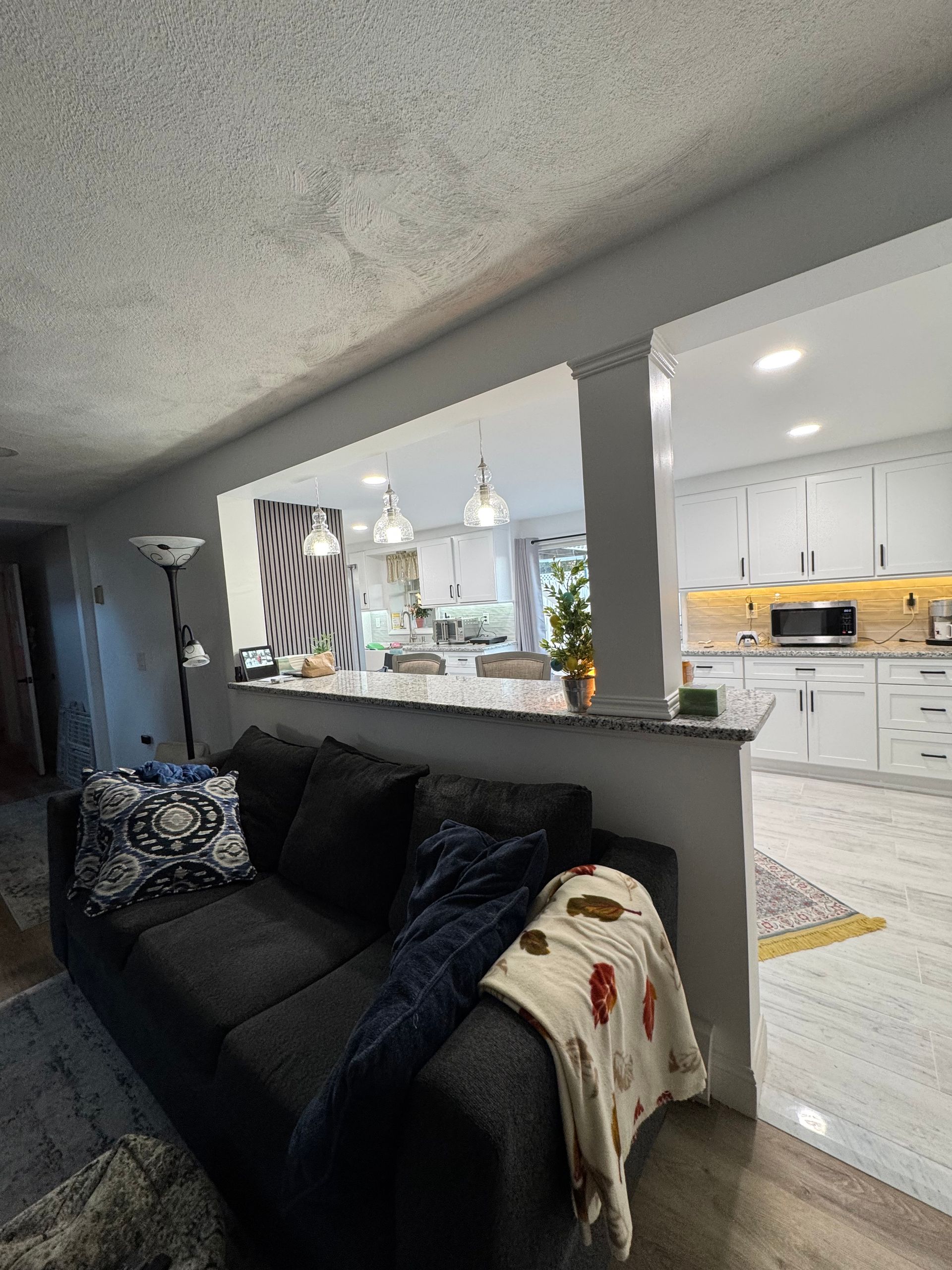 Living room view into a bright white kitchen with a dark sofa and gray half-wall divider