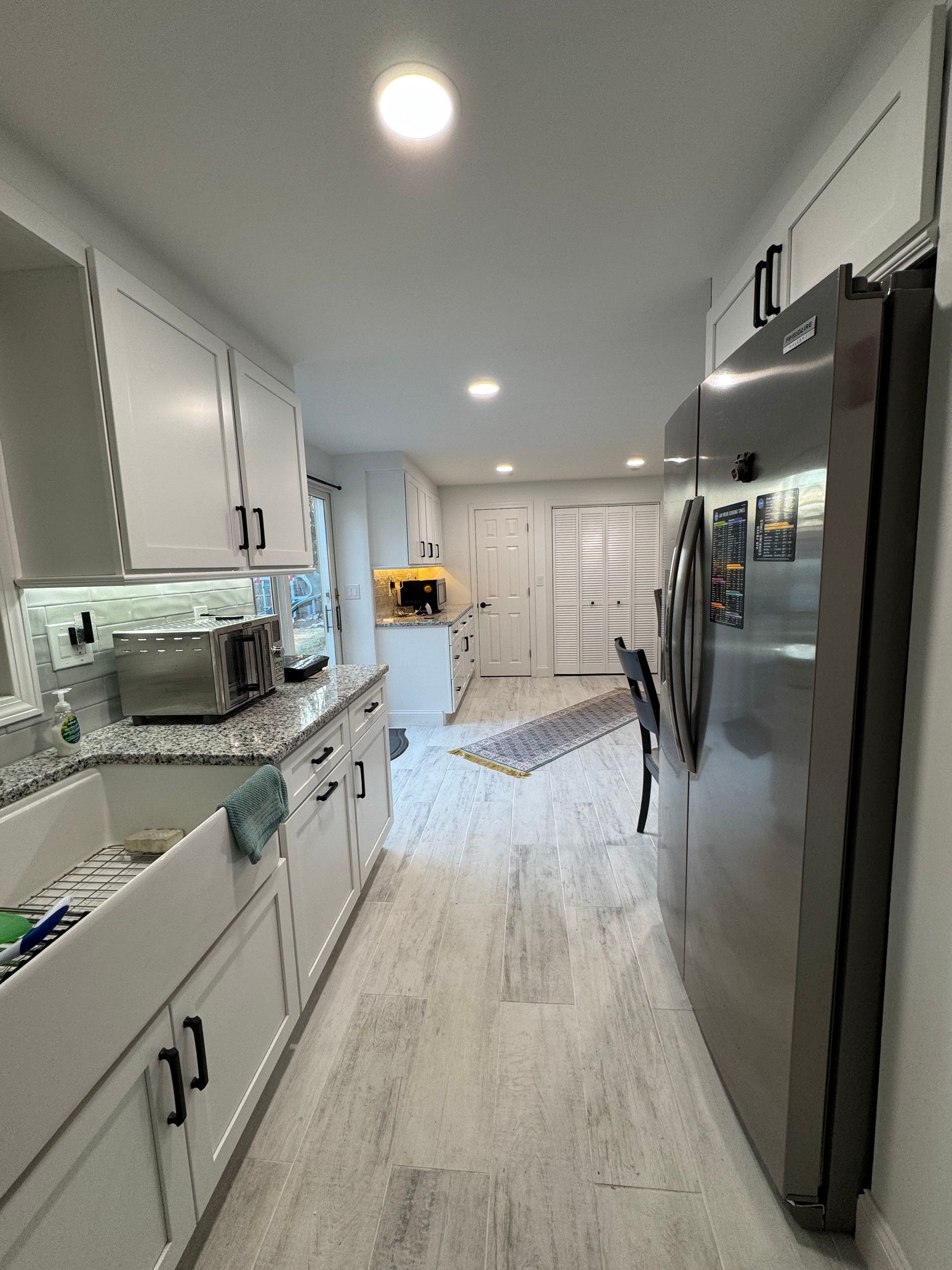 Bright white galley kitchen with stainless appliances, granite counters, and recessed ceiling lights.
