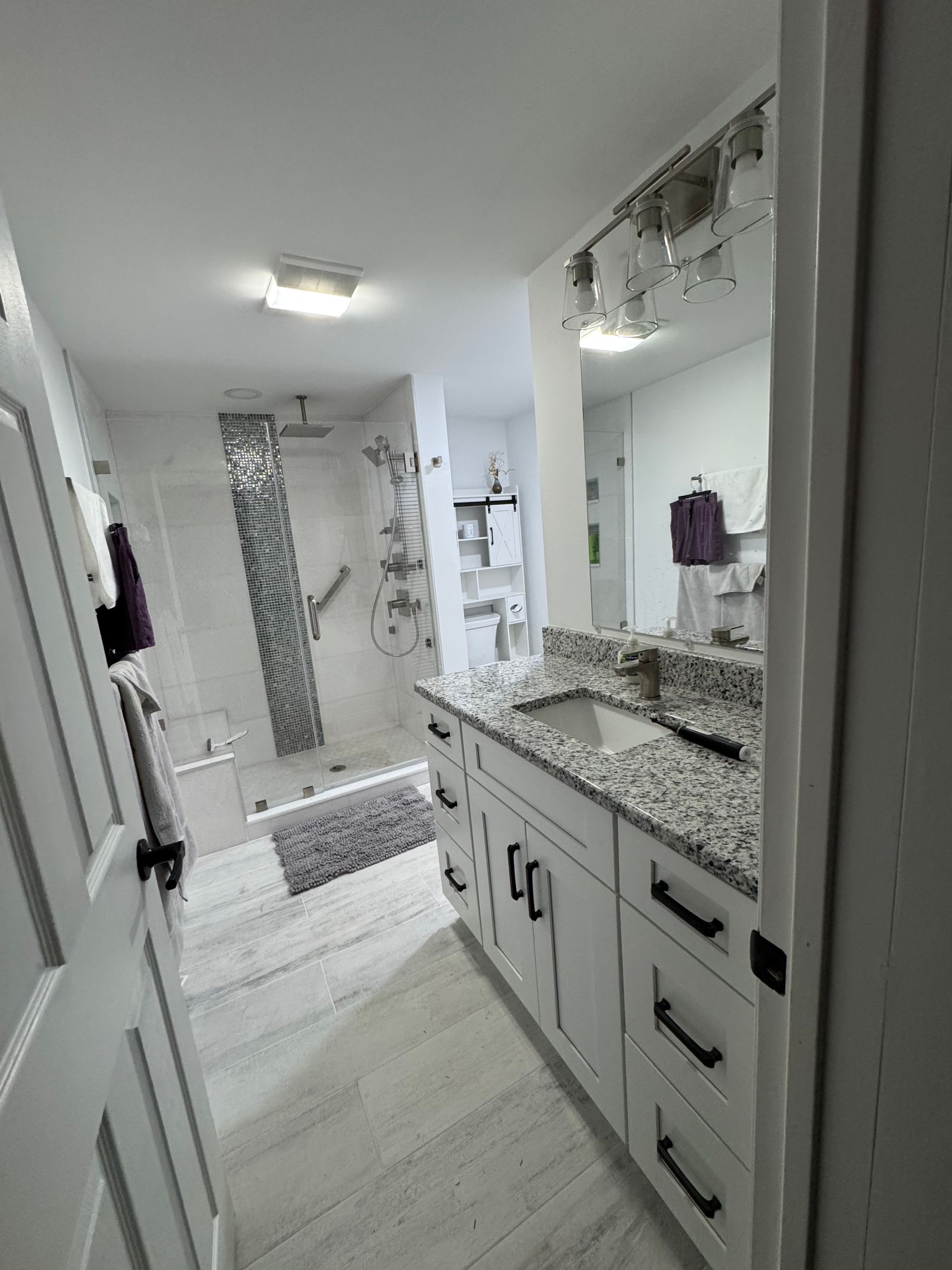 Bright bathroom with double vanity, large mirror, glass shower, and light tile flooring.
