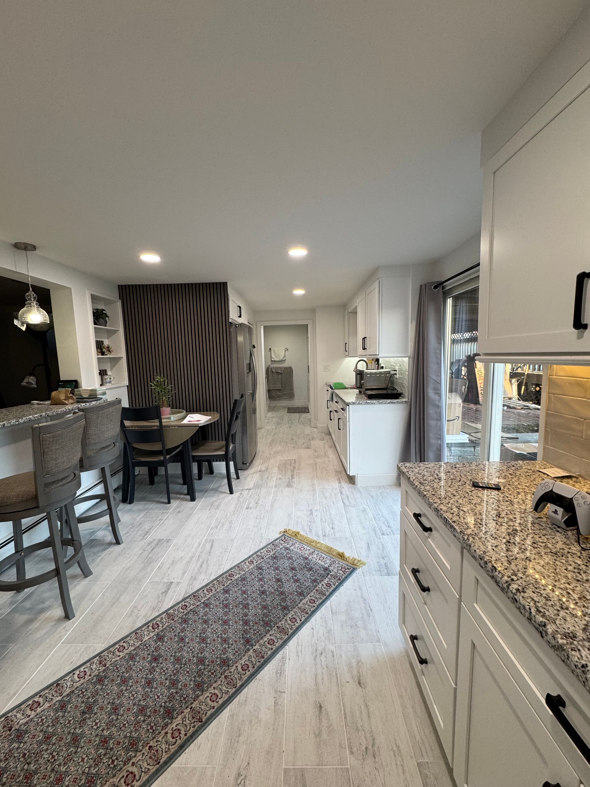 Bright kitchen opening to dining area, with white cabinets, granite counters, and a long runner rug.