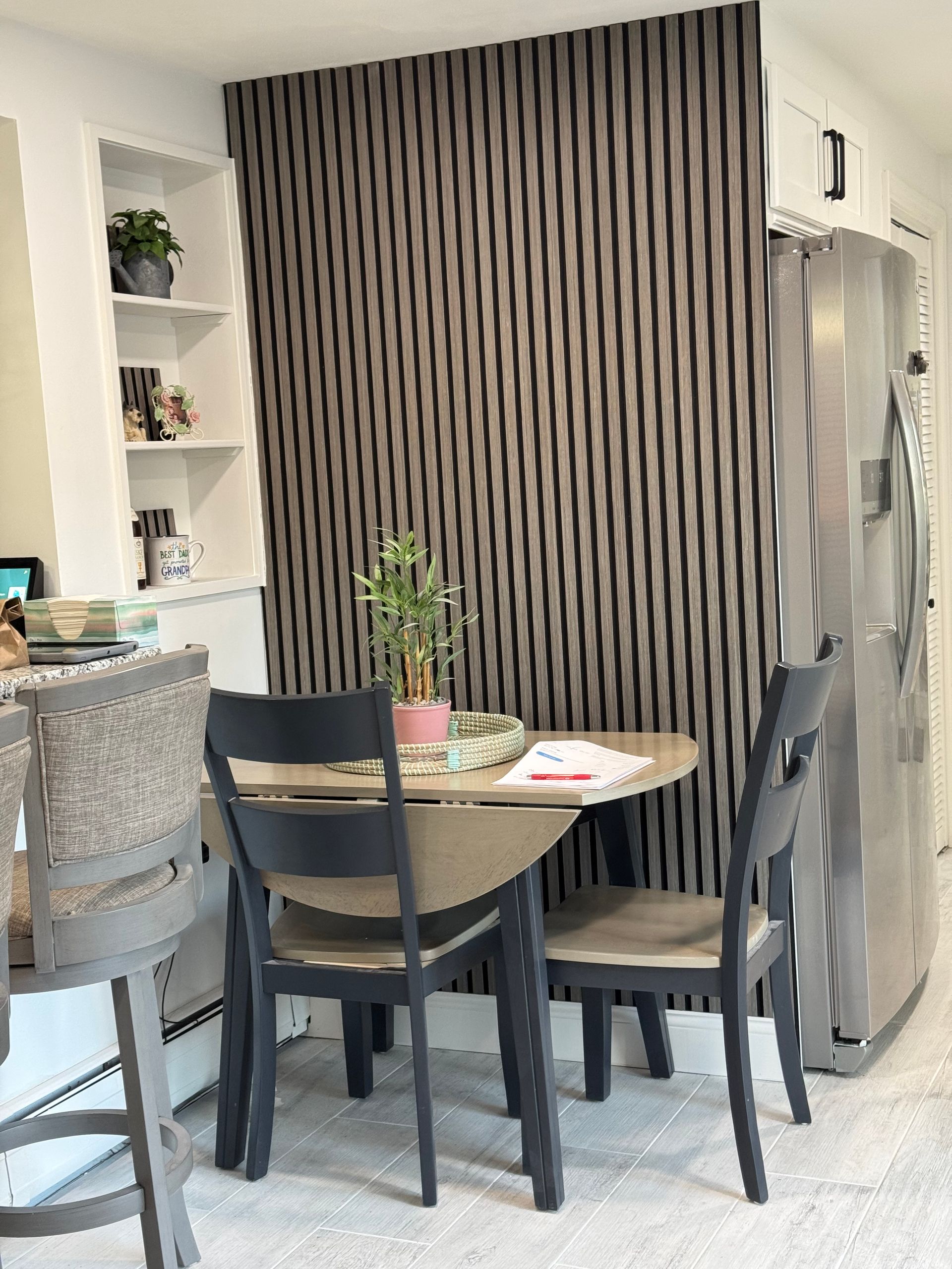 Modern kitchen nook with black chairs, round table, striped curtain, and stainless steel fridge