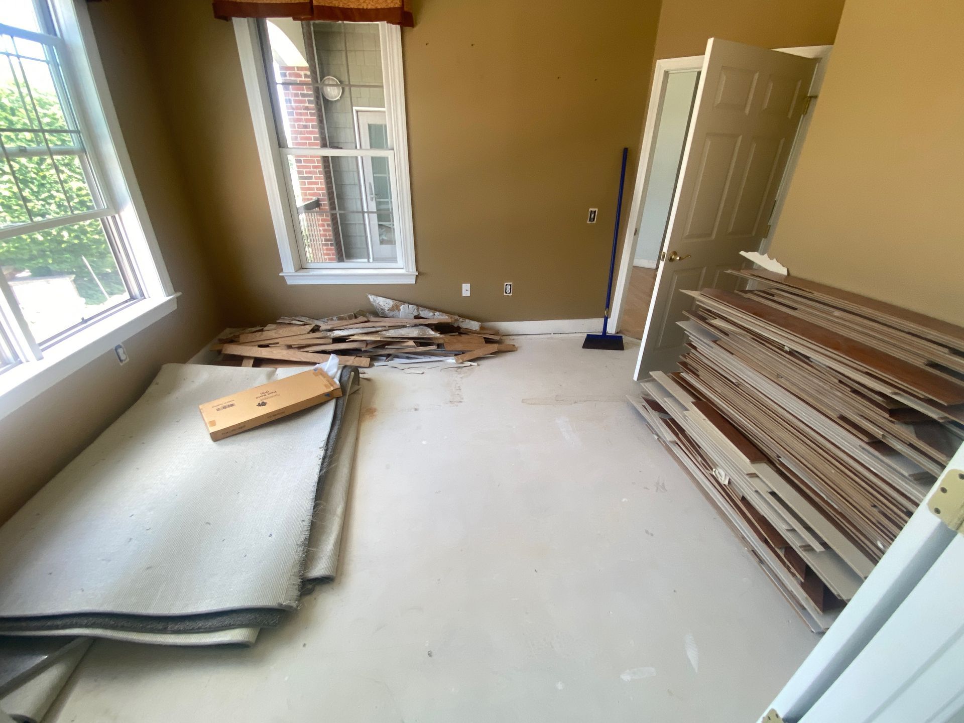 Partially renovated room with drywall, lumber, and debris stacked by the wall near the windows